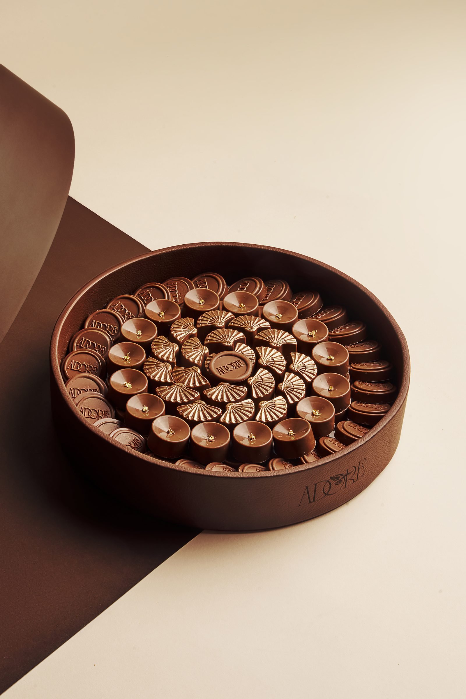 Round box of moulded chocolates arranged in a spiral on a cream backdrop