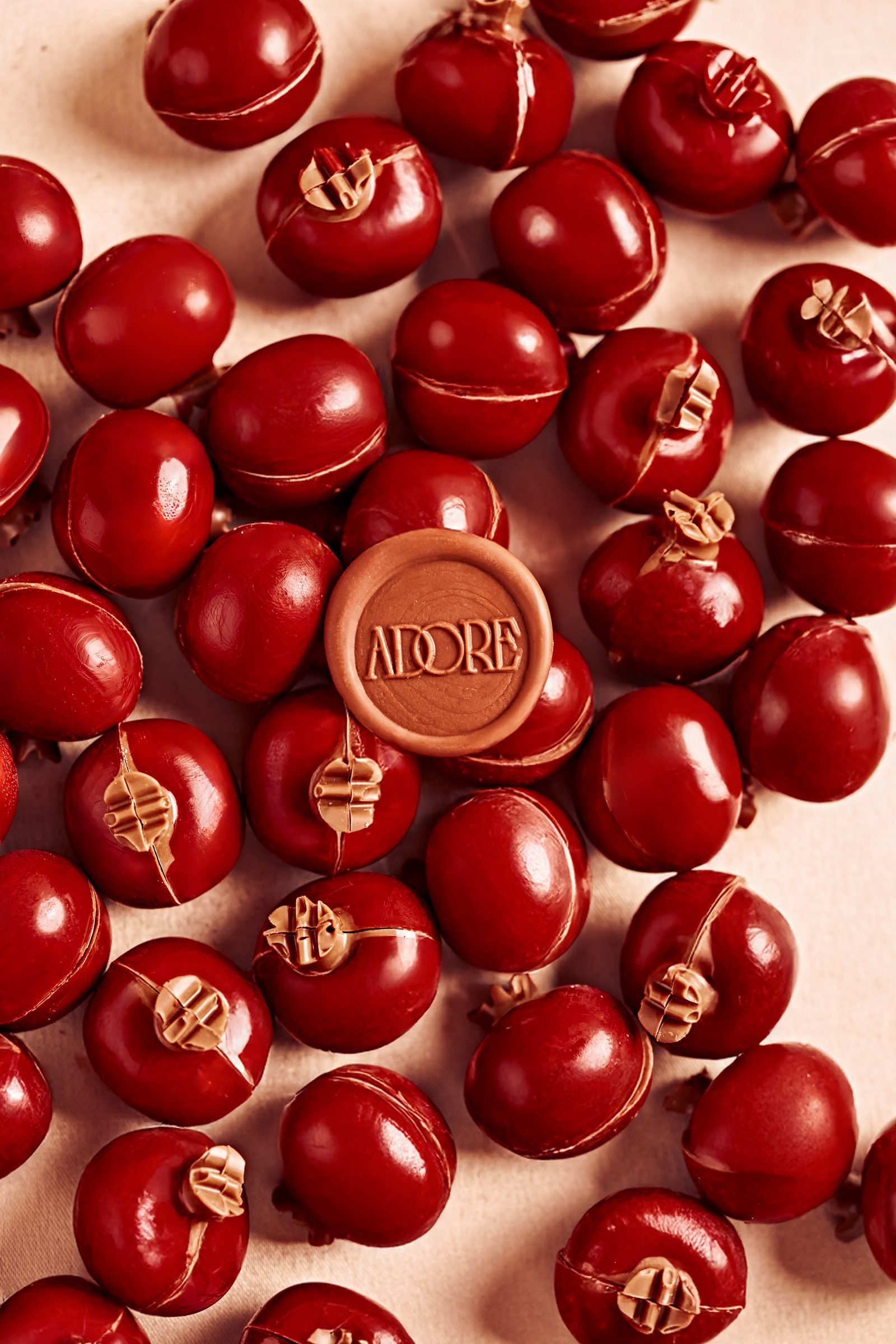 Glossy red chocolate spheres around a single Adore-stamped disc