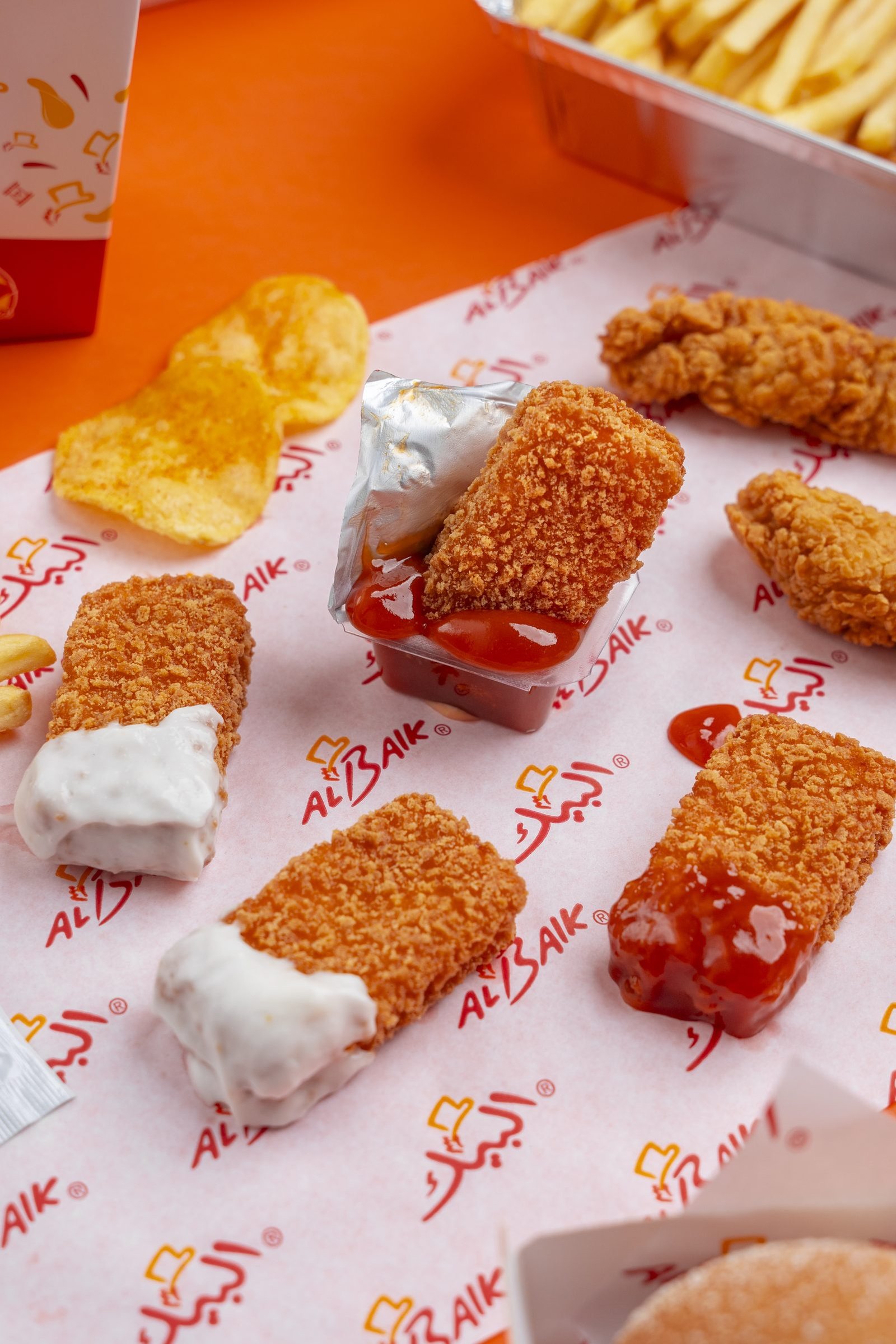 Fried chicken fillets, nuggets and crisps on Al Baik paper with dips, on orange