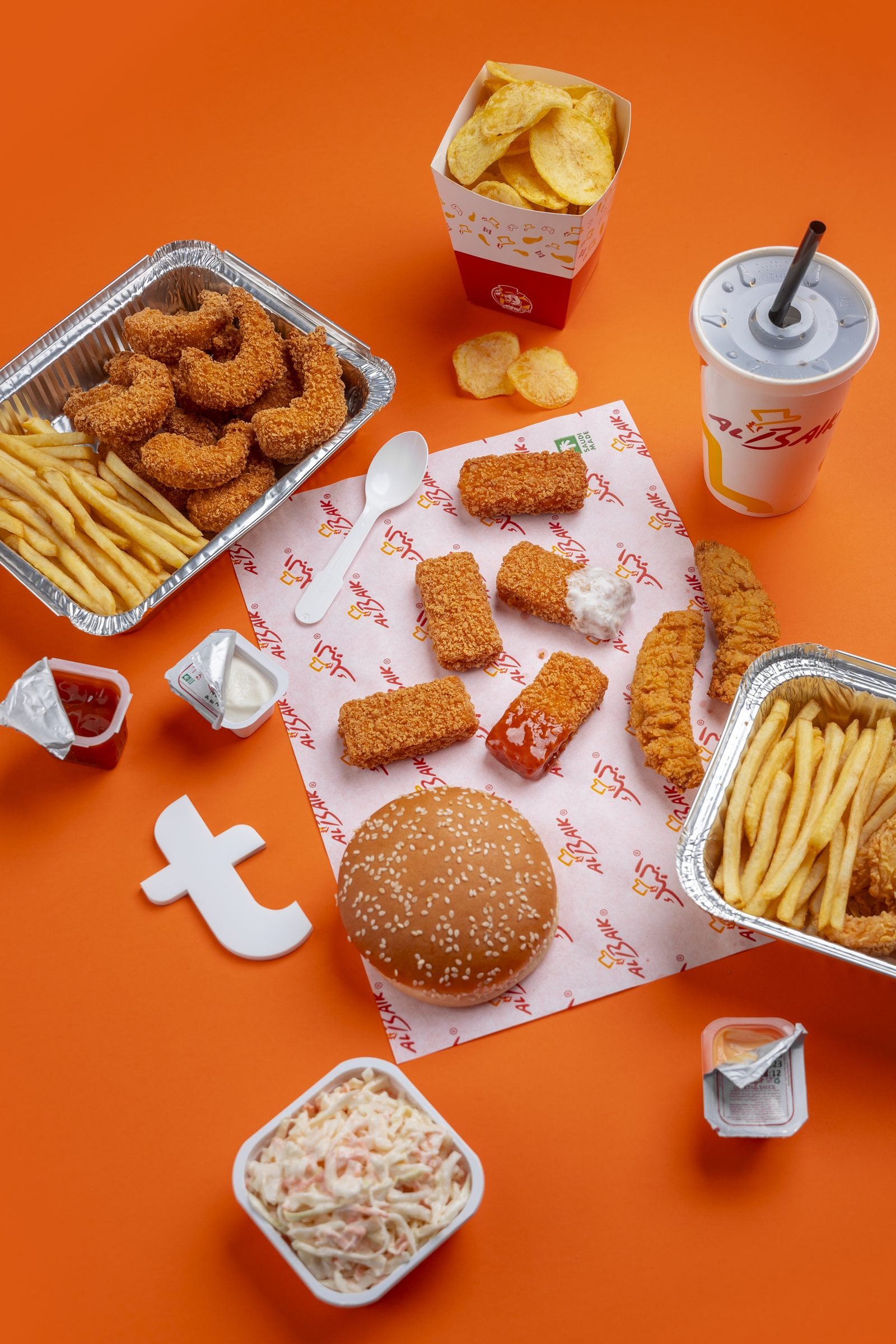 Overhead Al Baik meal of nuggets, fries, a burger, coleslaw and a drink on orange