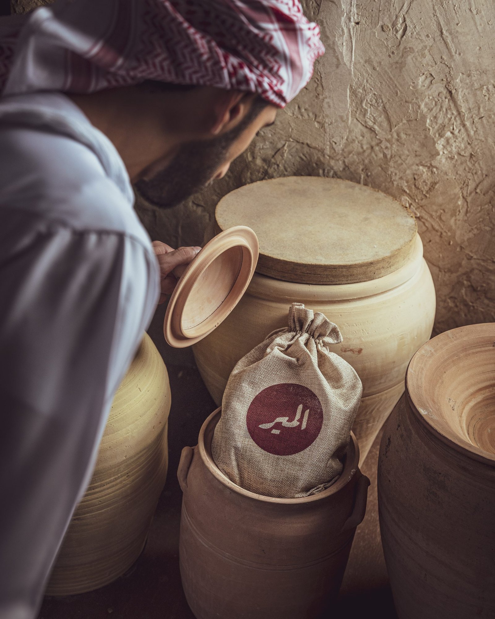 Woman lifting the lid of a clay storage jar beside sacks stamped with the Almair mark