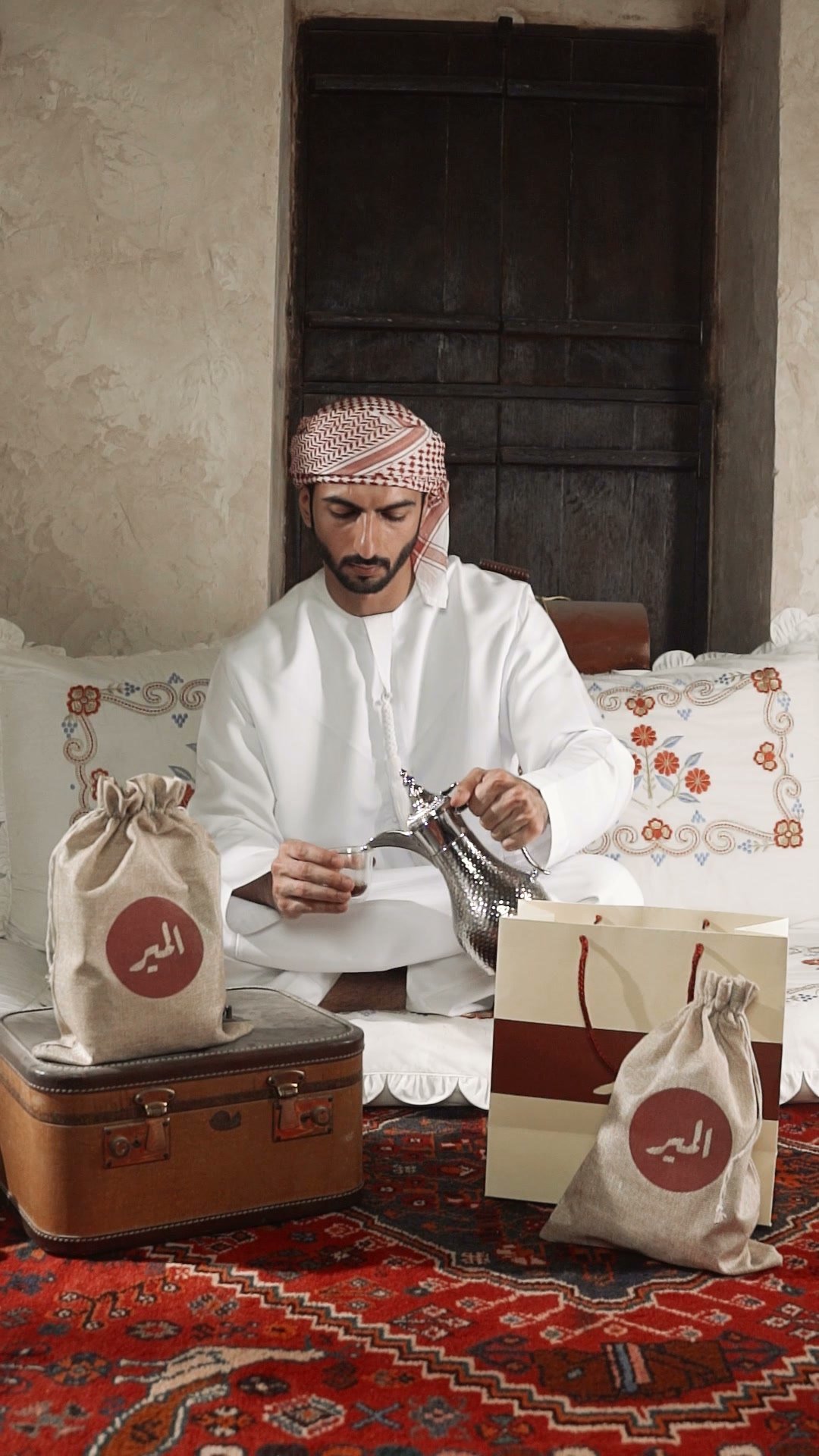 Man in a kandura seated on a carpet packing Almair coffee sacks into a case