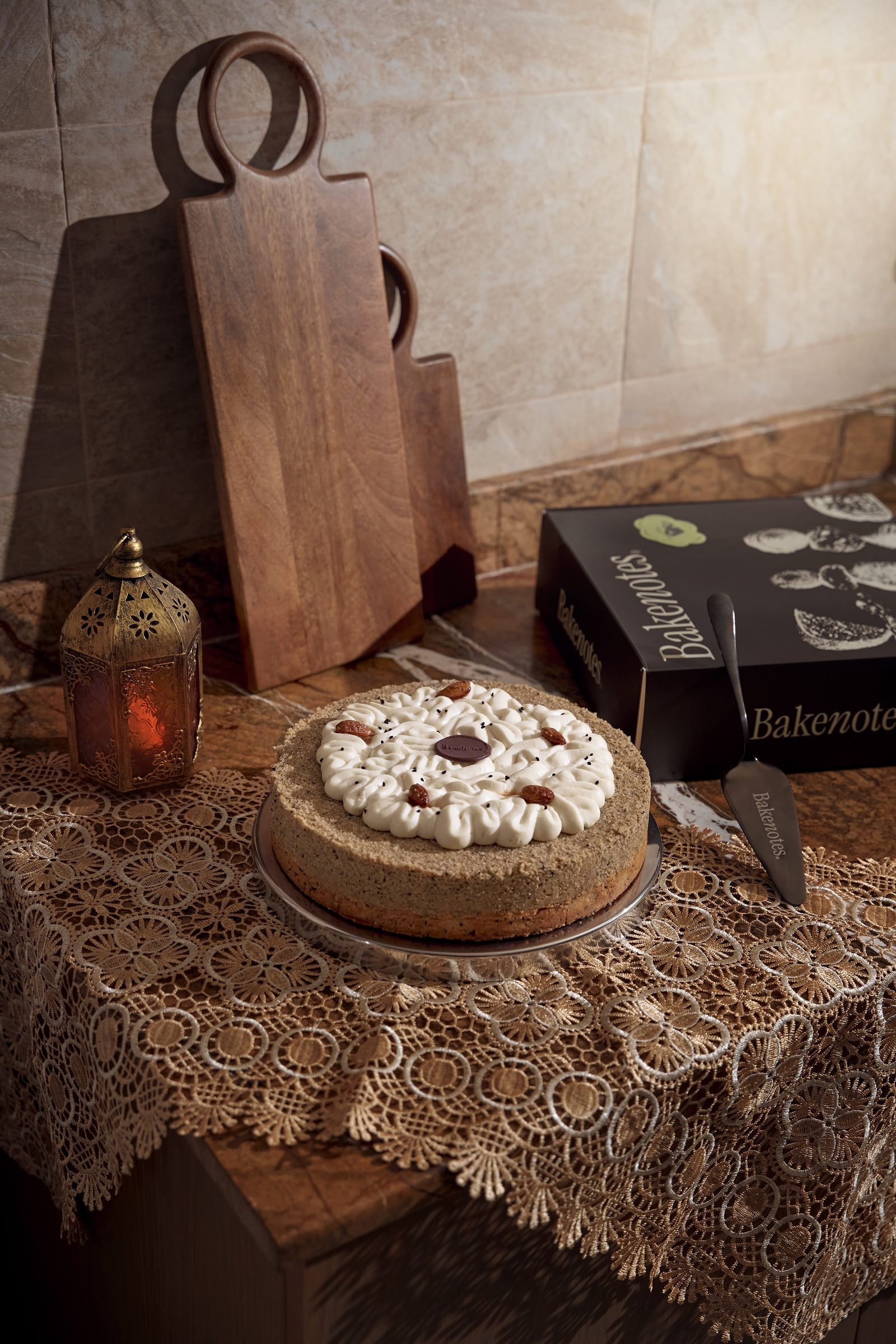 Round cake topped with nuts on a lace tablecloth beside wooden serving boards and a brass lantern