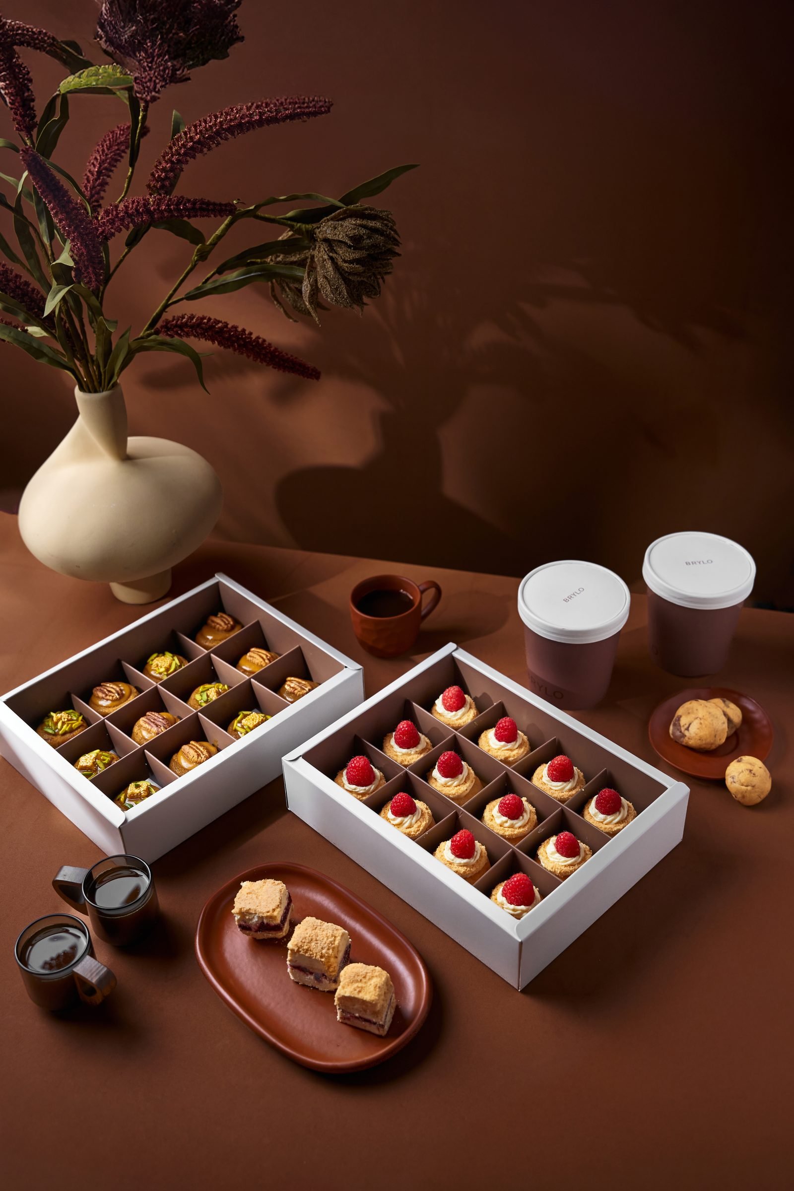 Two open boxes of pistachio and berry bites on a brown set with a vase of dried flowers