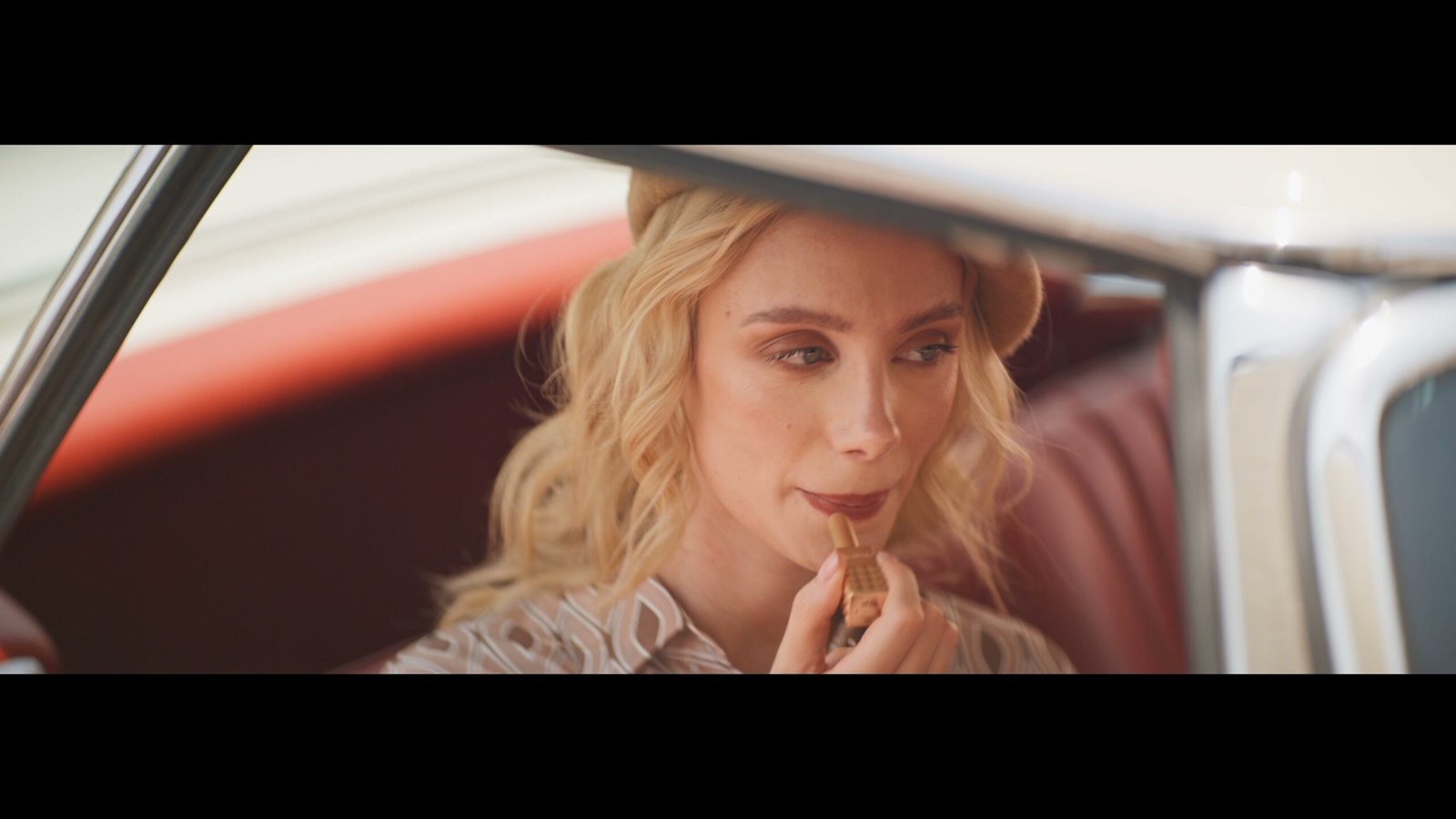 Woman in a car applying lipstick, framed as a widescreen film still