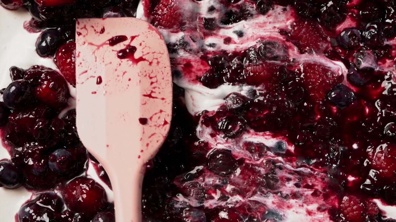 Spatula folding cream through crushed blackberries and raspberries