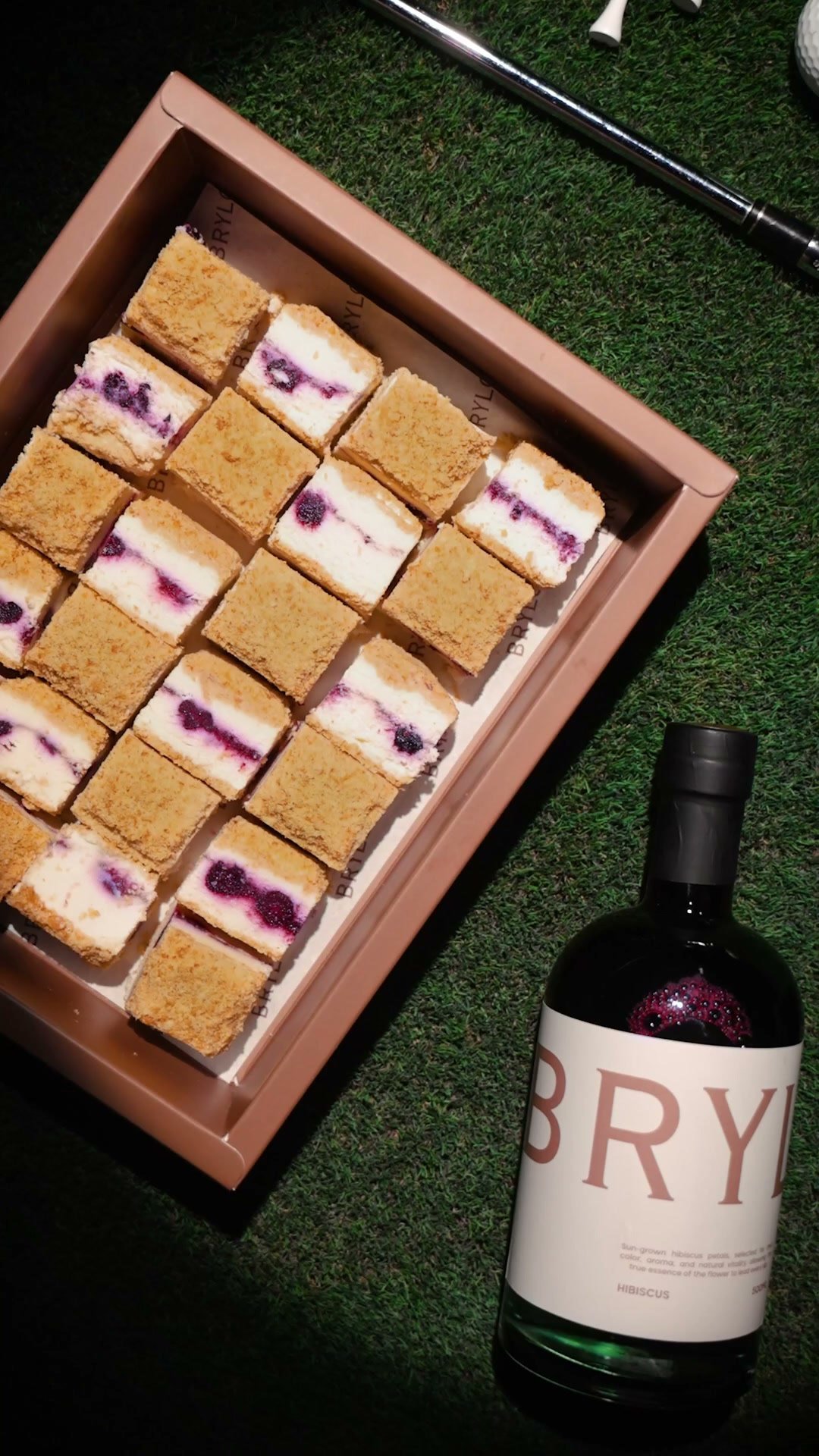 Tray of berry cheesecake squares on grass beside a bottle of Brylo