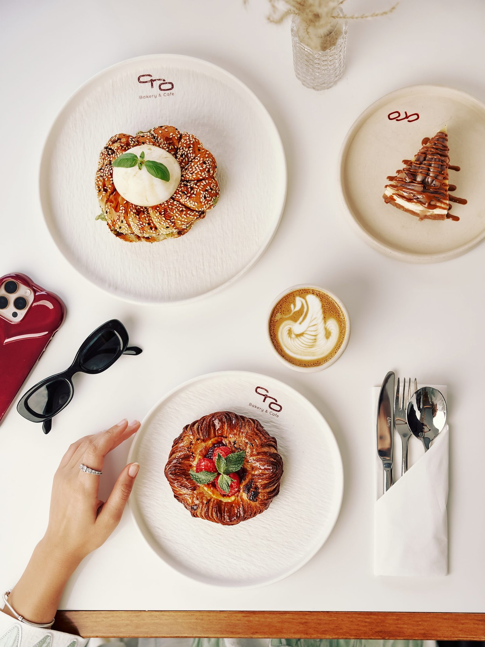 Overhead cafe table with two pastries, a latte, sunglasses and a phone on white