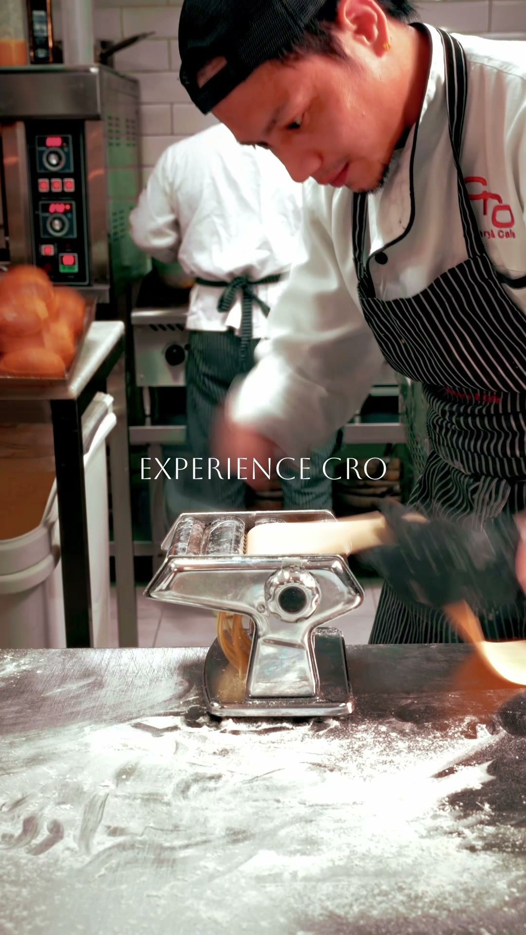 Baker in a Cro apron rolling dough on a floured steel bench