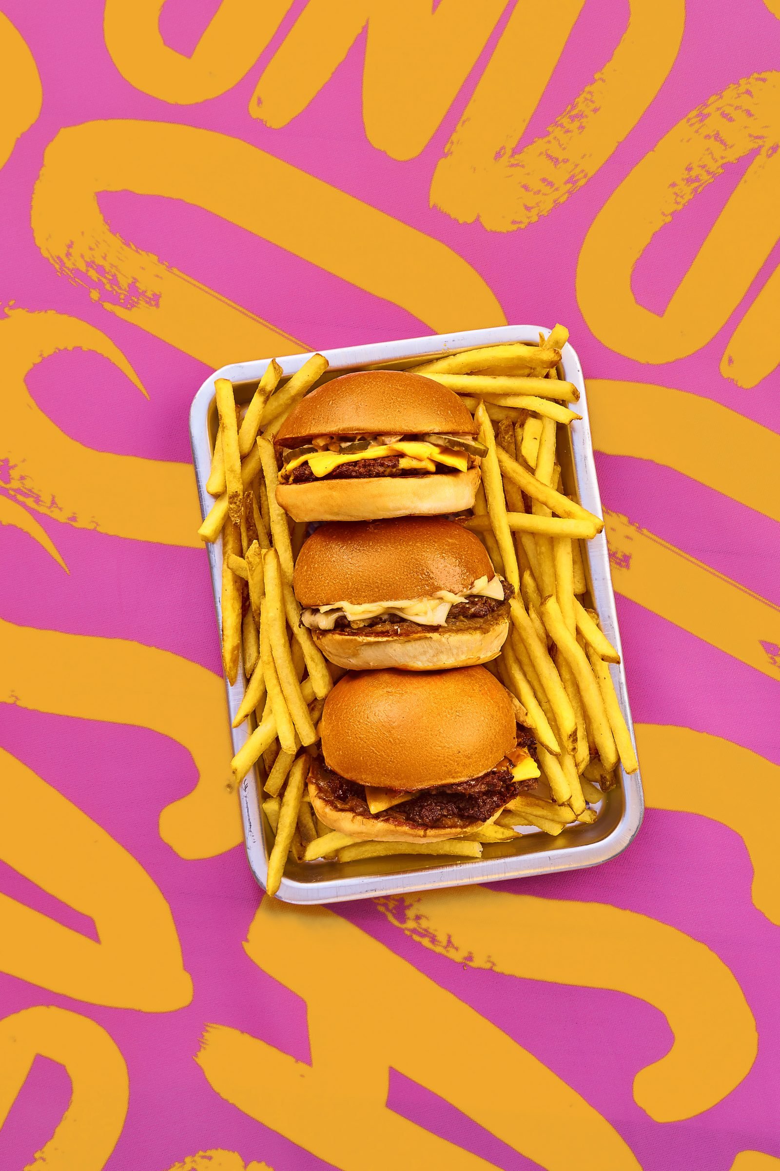 Cheeseburger and fries in a foil tray on a pink and yellow painted backdrop