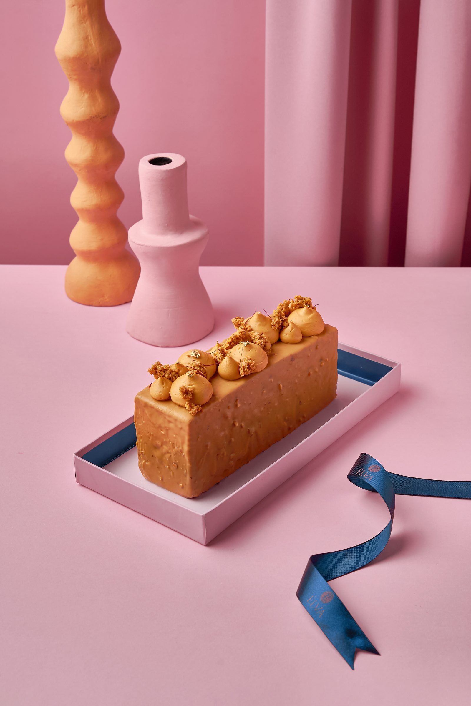 Caramel-topped loaf cake on a pink tray against pink curtains, a navy ribbon trailing