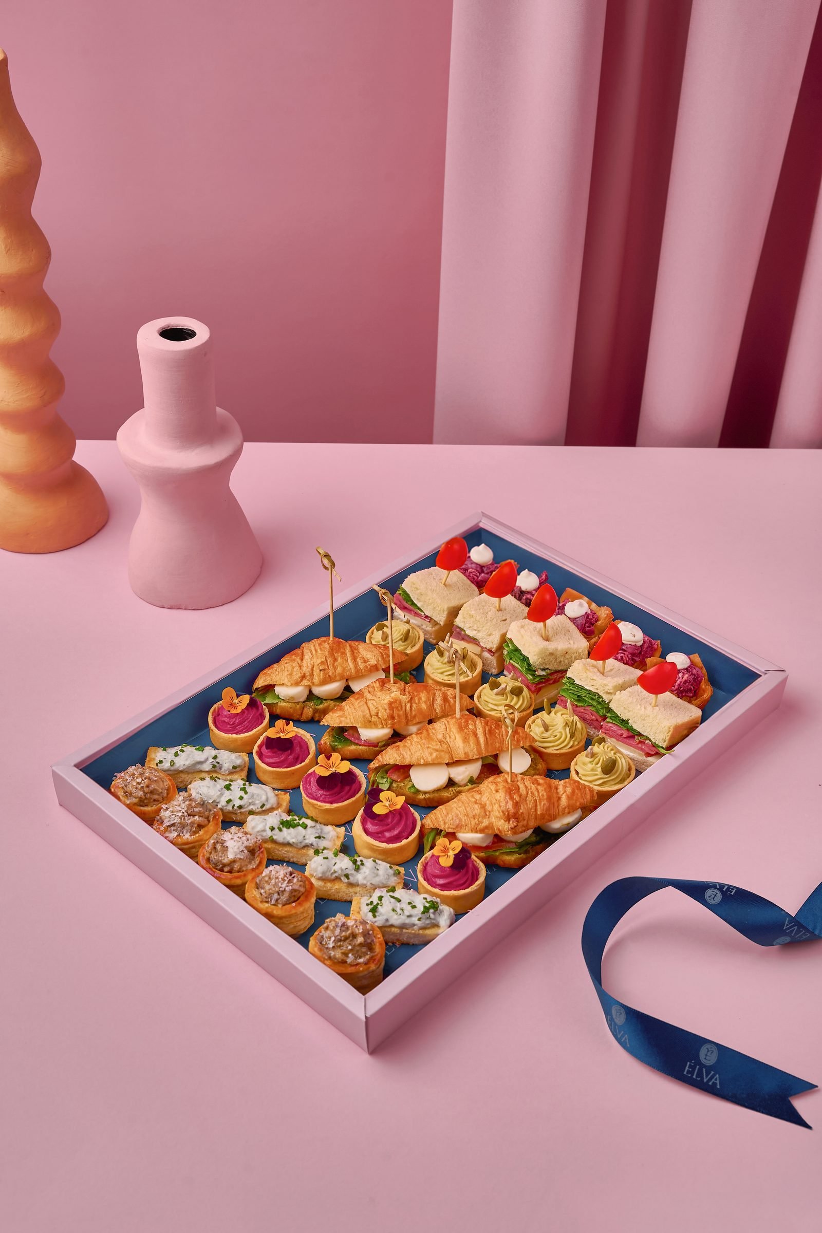 Tray of assorted canapes and mini pastries on a pink set with a navy ribbon