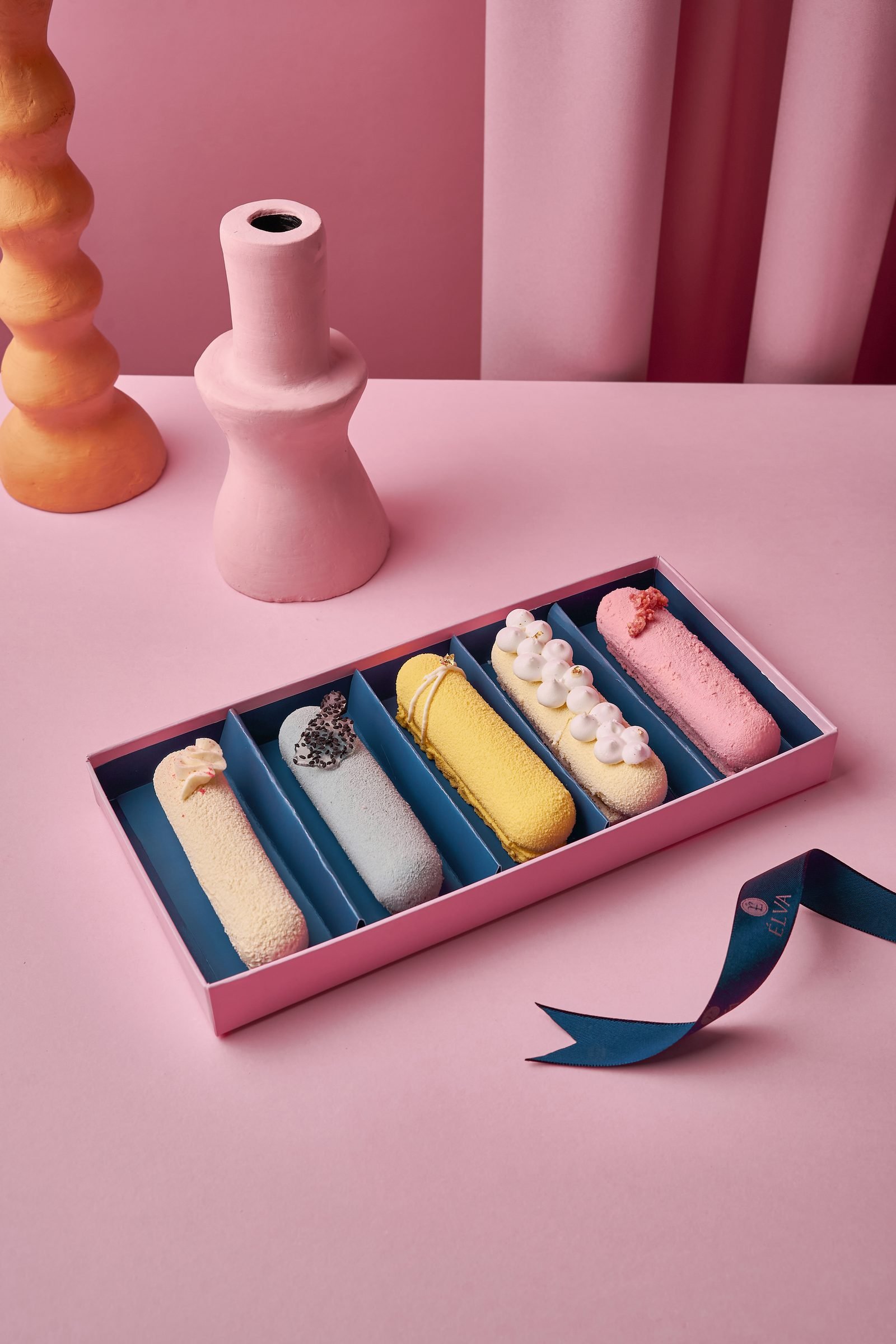 Box of five glazed eclairs in different colours on a pink set with a navy ribbon