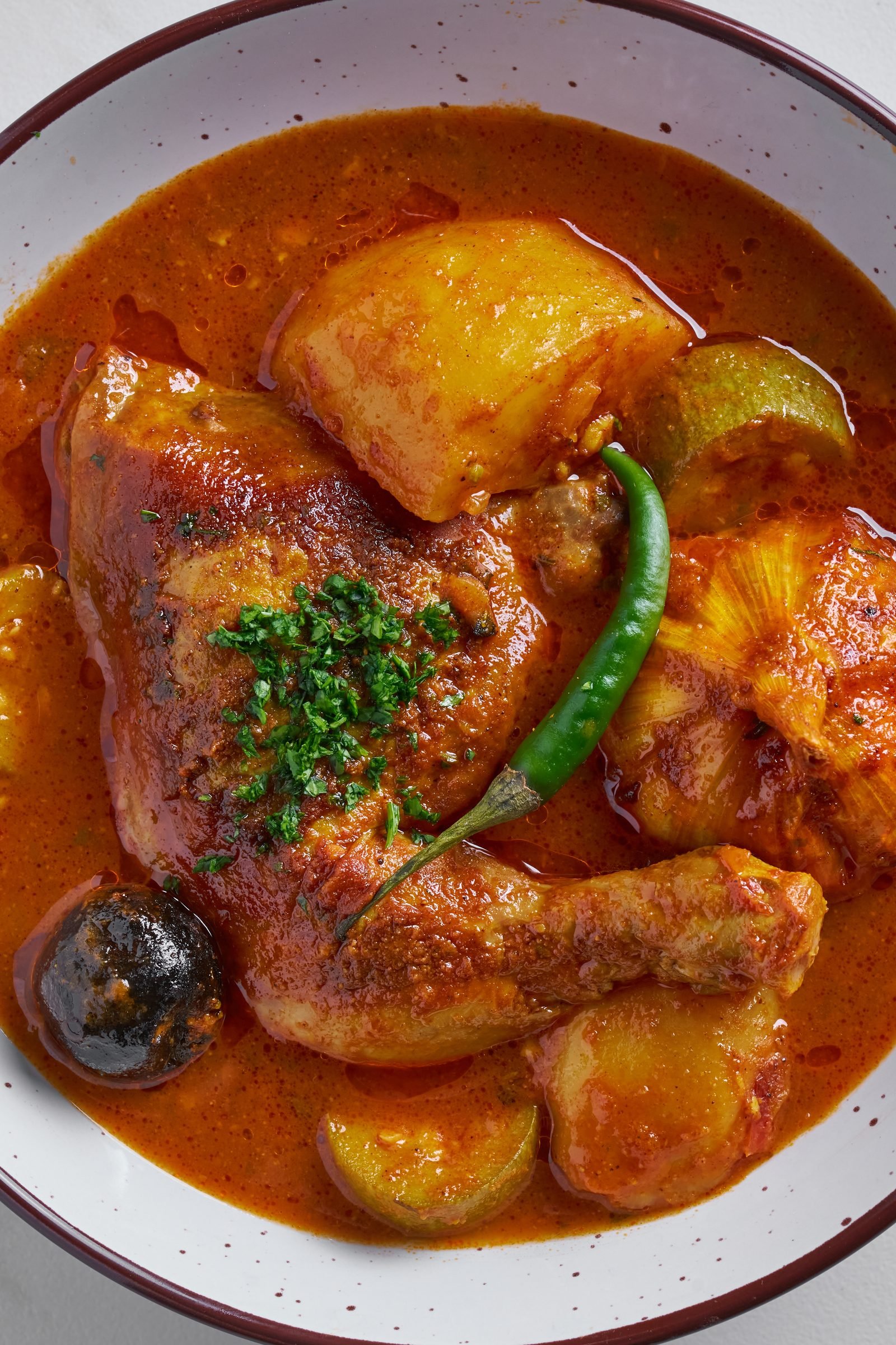Chicken and potato stew in tomato sauce with a green chilli and dried lime on a rustic plate