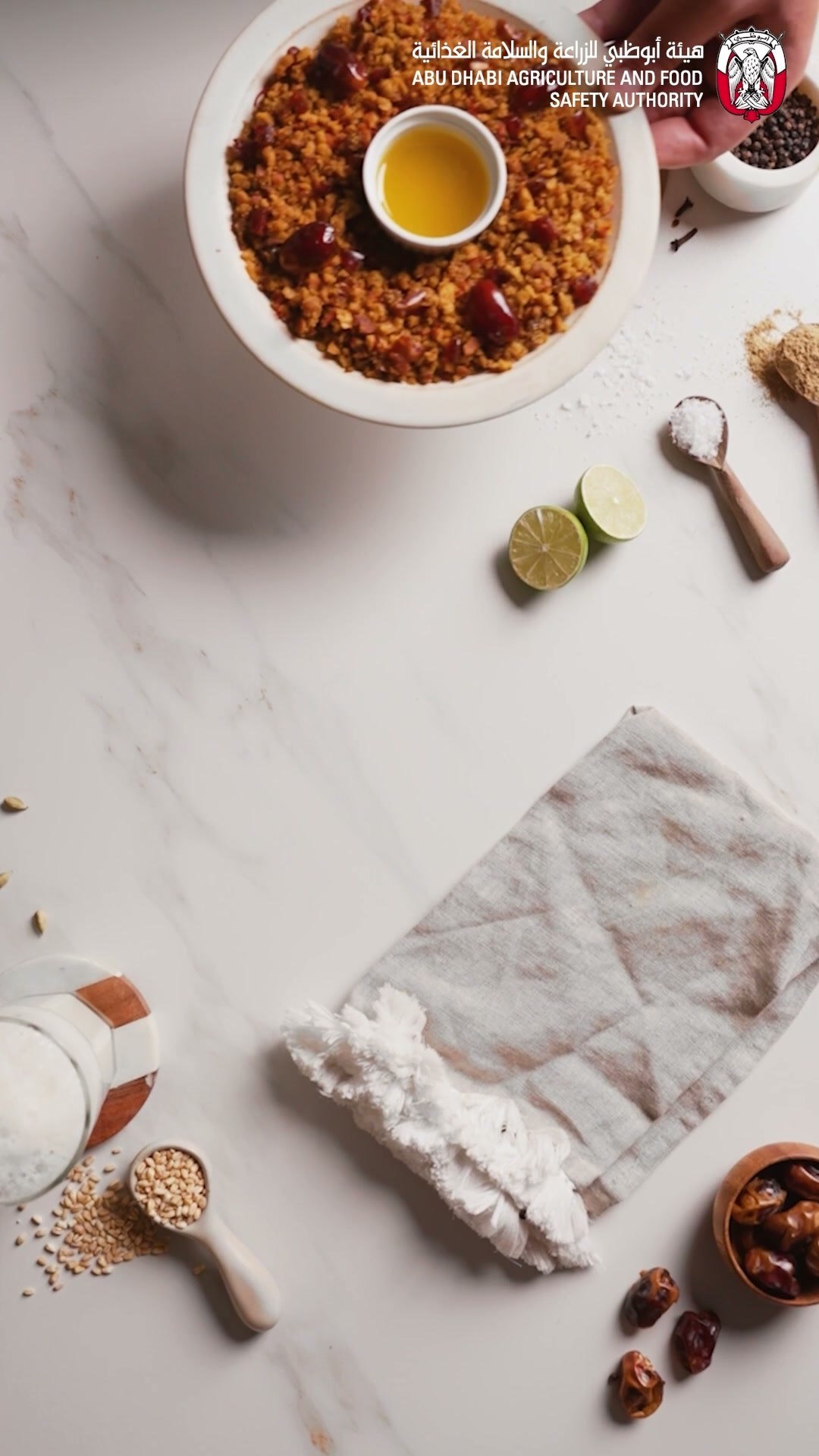 Overhead of spiced rice with a bowl of ghee, dates and sesame seeds beside a linen cloth on marble