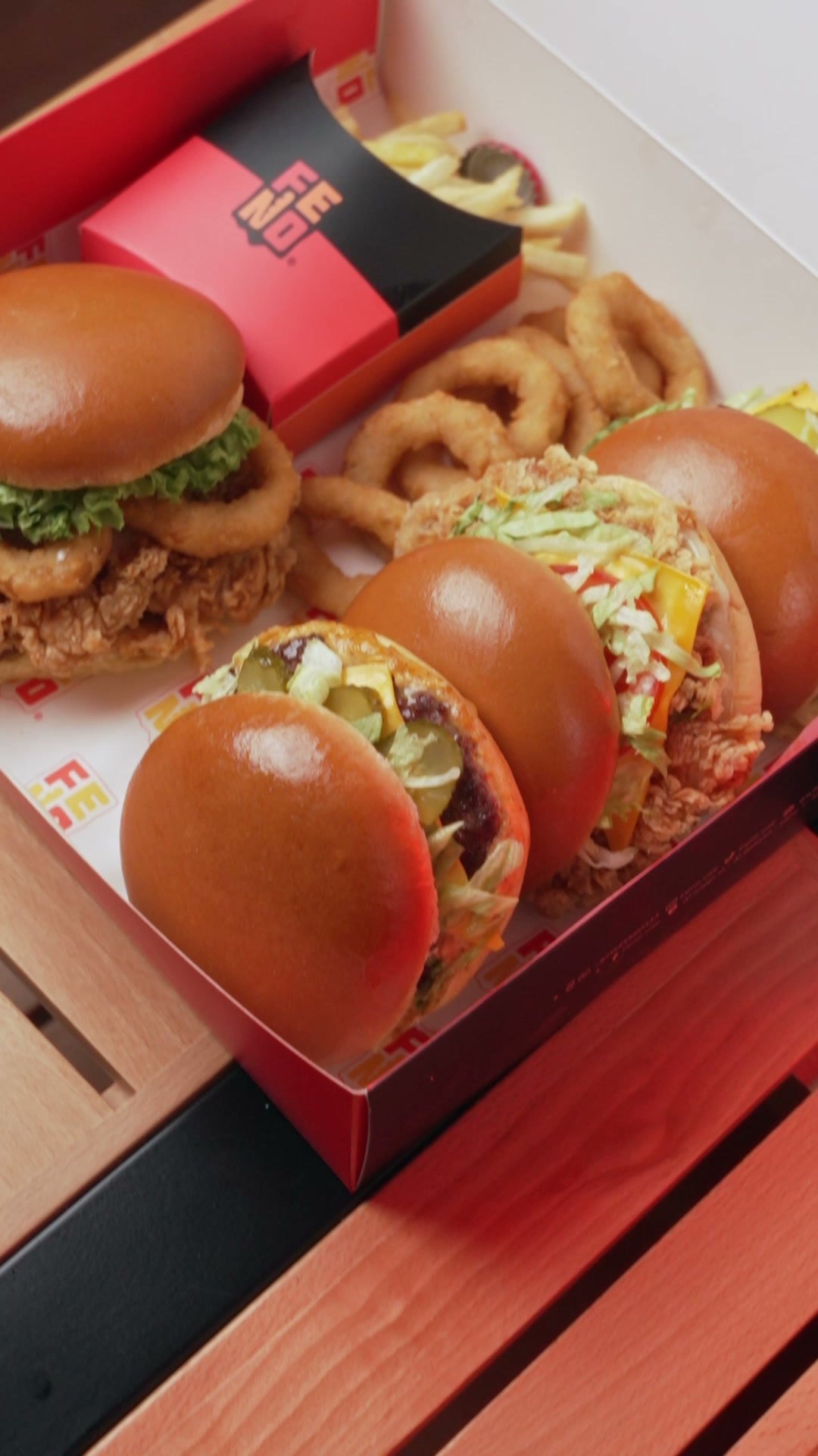 Fried chicken burgers and onion rings in an open Fino box on a red table