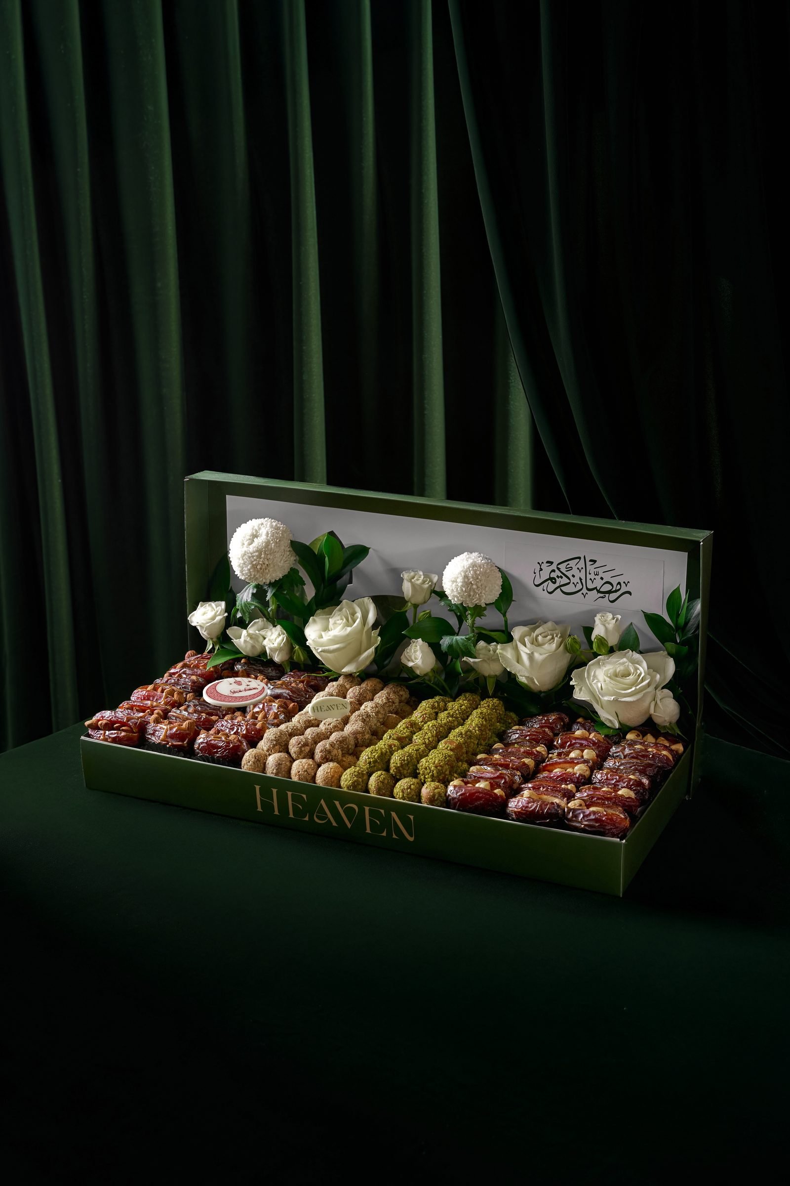 Long box of dates and chocolates dressed with white roses, on dark green