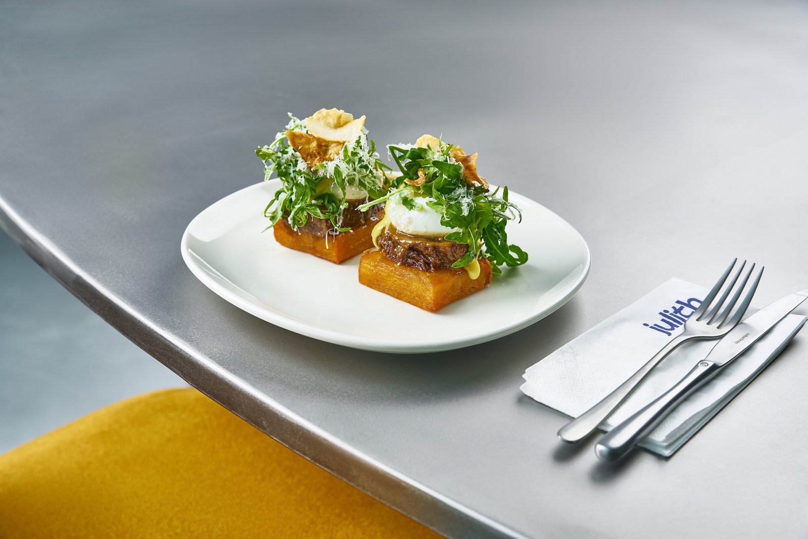 Two open sandwiches with poached egg and greens on a white plate on a steel counter