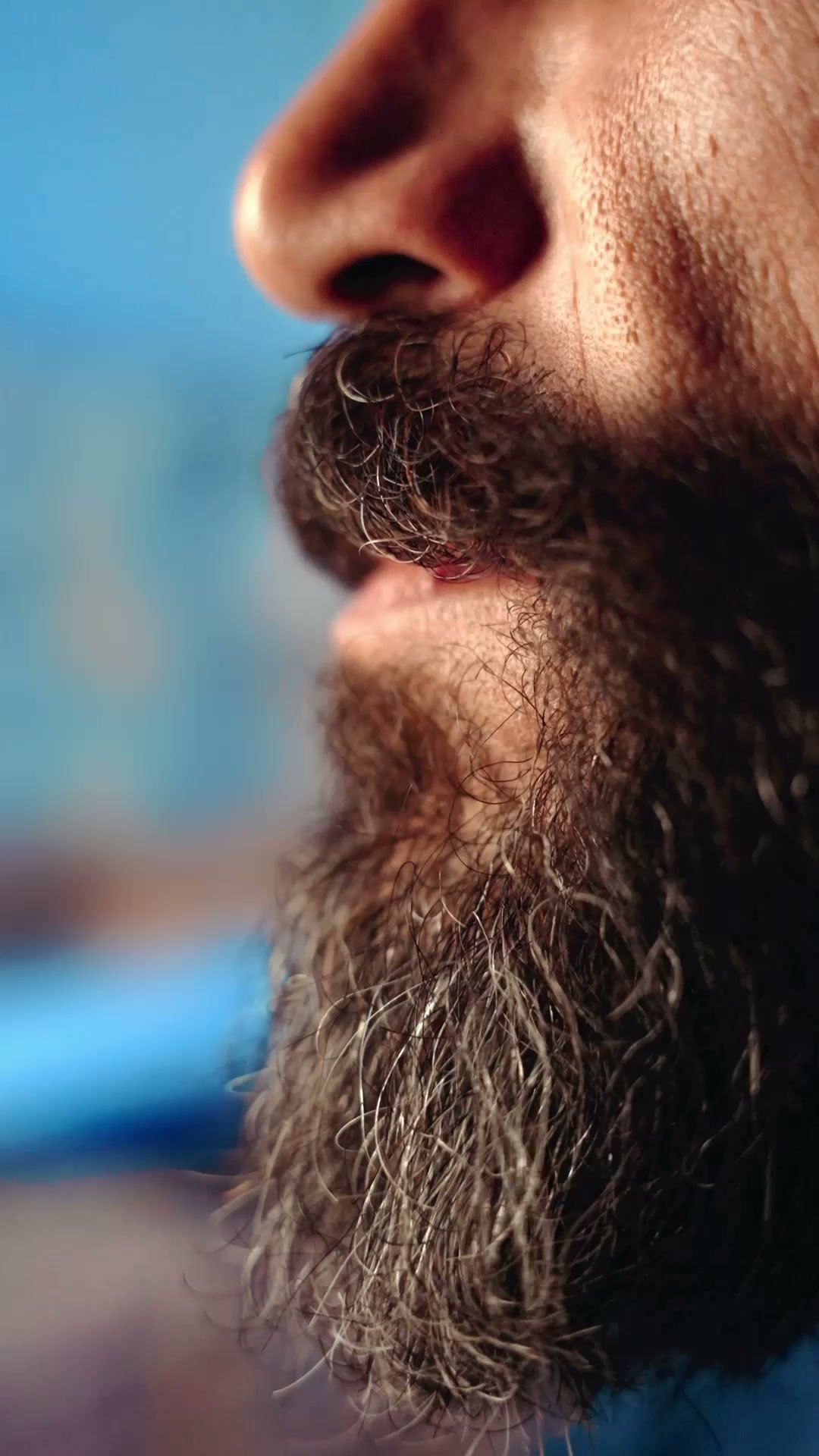 Close-up of a bearded man's mouth and chin in profile against blue