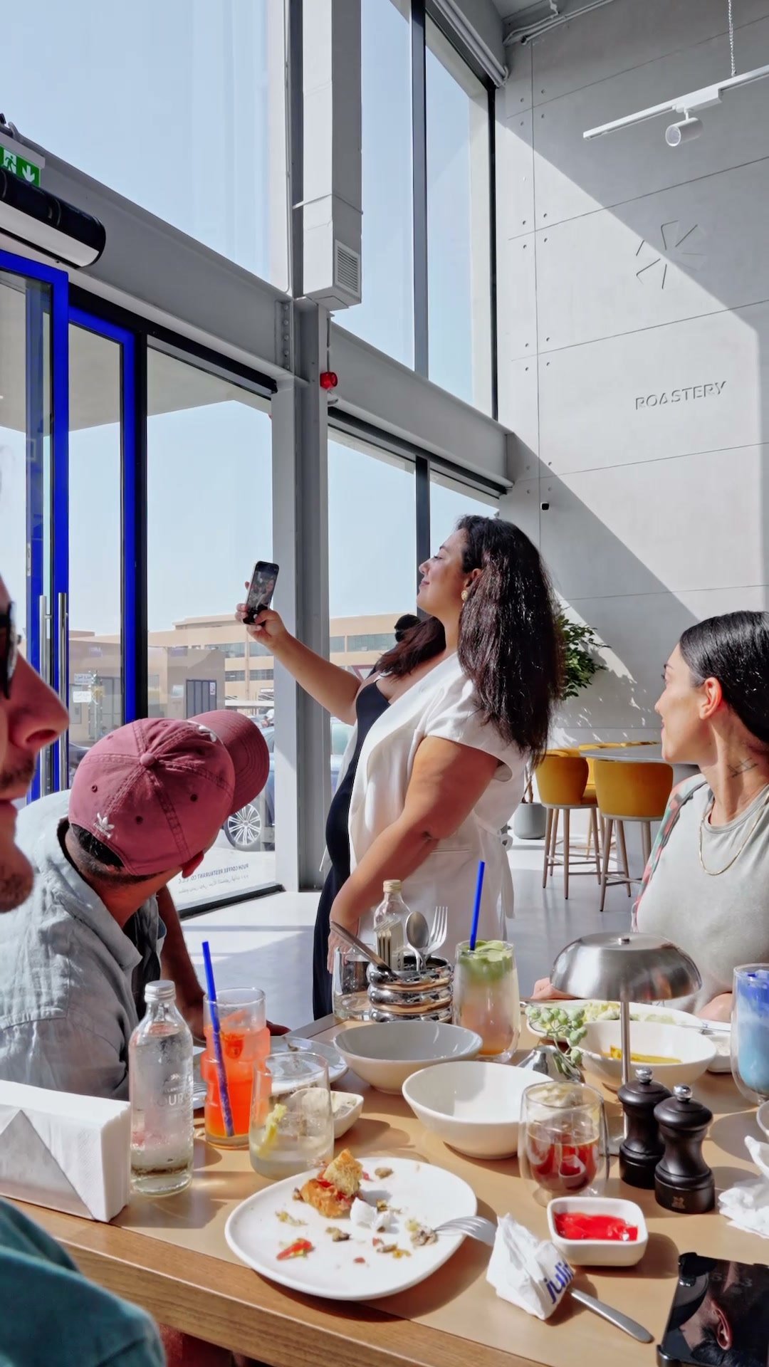 Diners at a long window table taking photographs, city light behind them