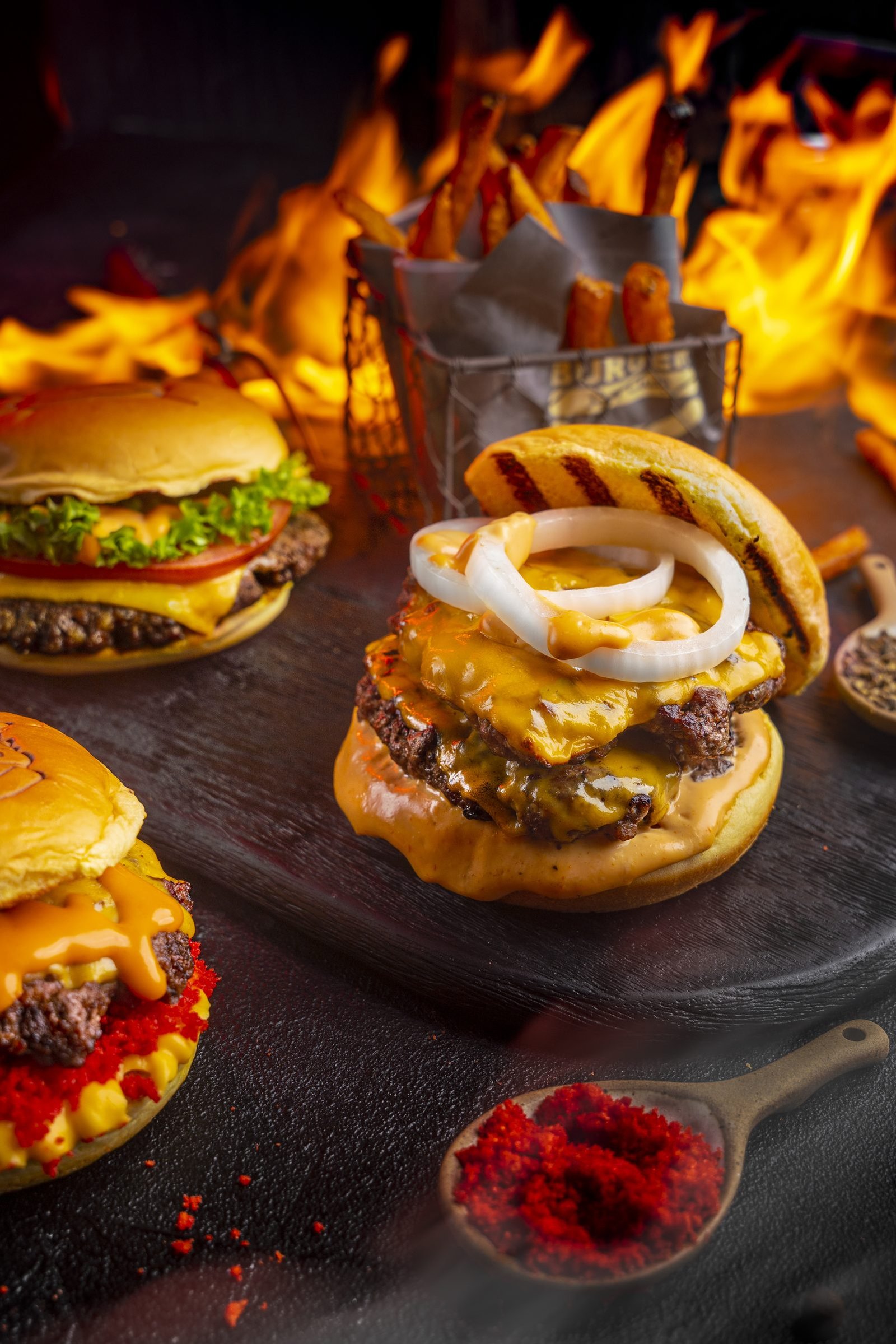 Stack of cheeseburgers with onion rings and fries against a wall of flame