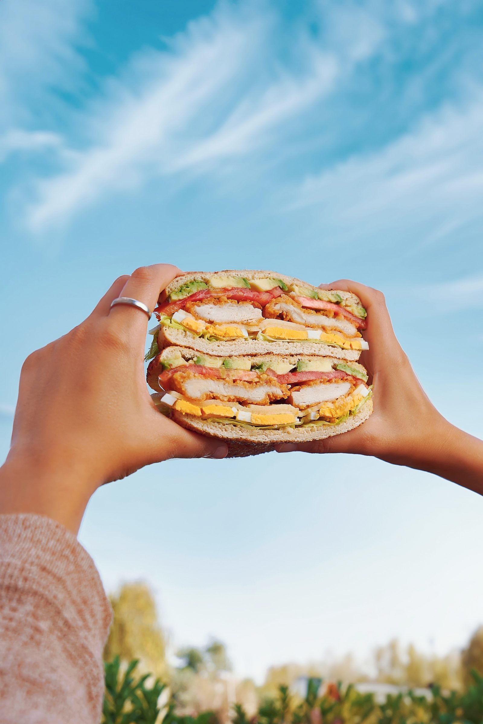 Hands holding up a stuffed kaak flatbread against a bright blue sky