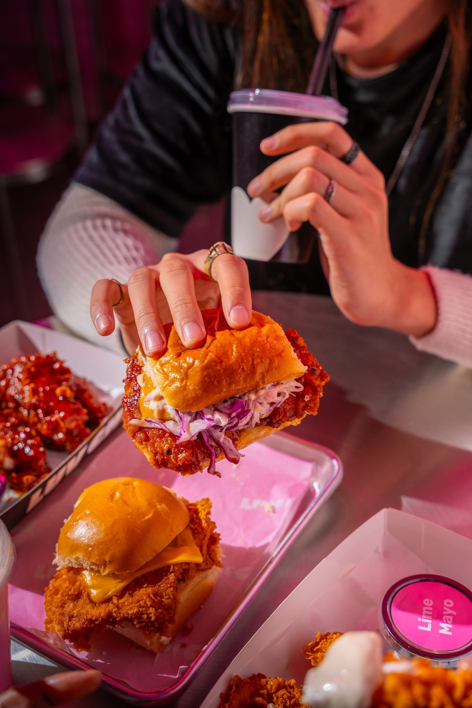 Two people sharing fried chicken sandwiches and hot wings on a pink tray