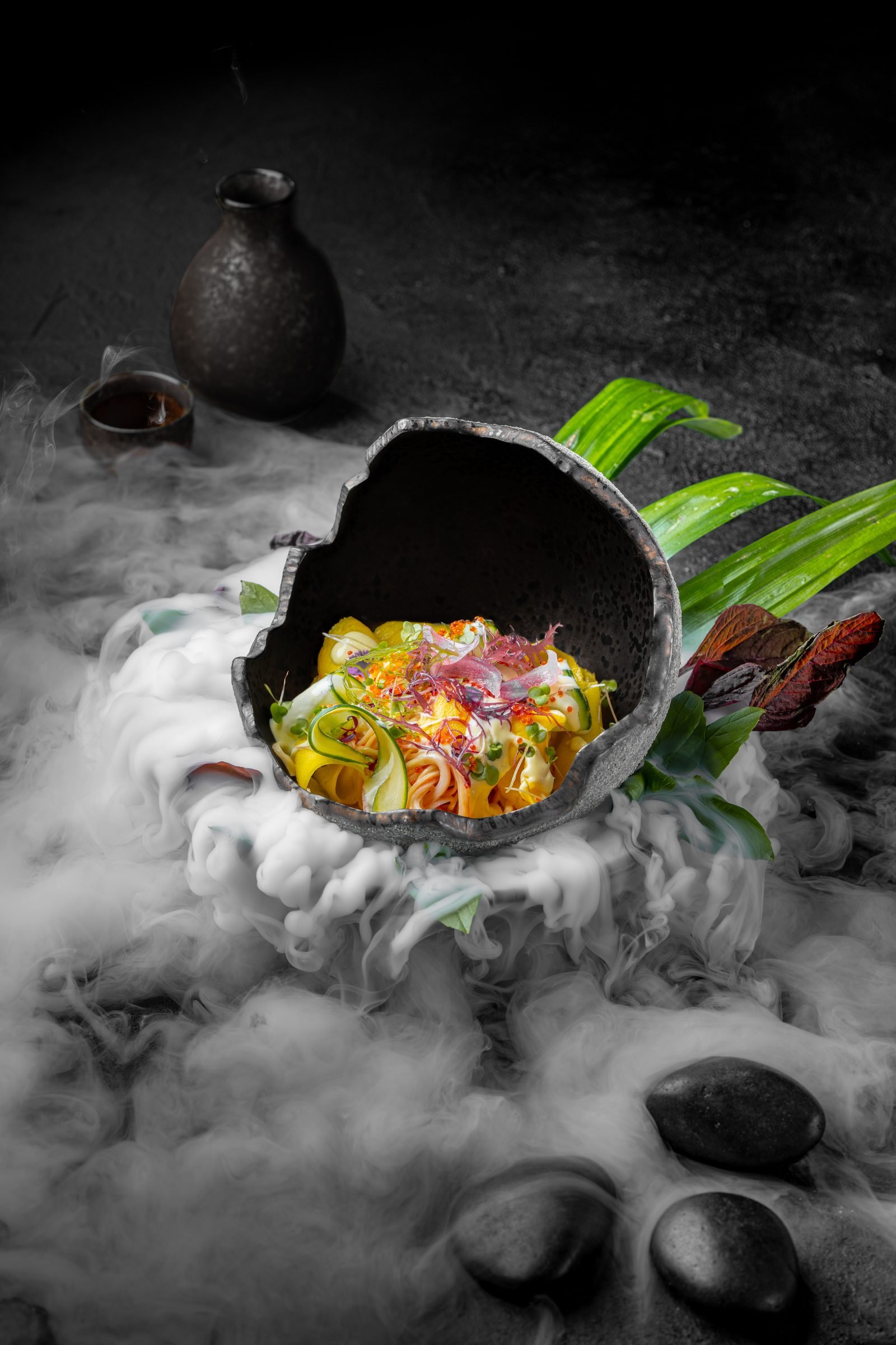 Sushi salad in a cracked black stone bowl, dry ice spilling over the slate beneath