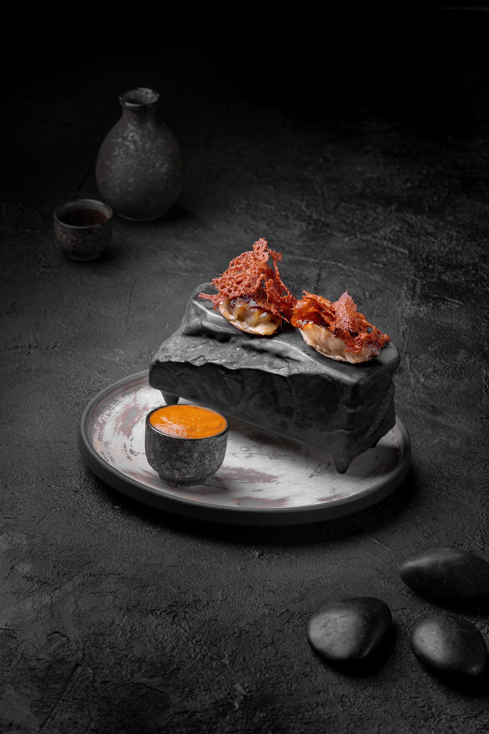 Seared fish on a black rock plate with a dipping sauce, surrounded by smoke