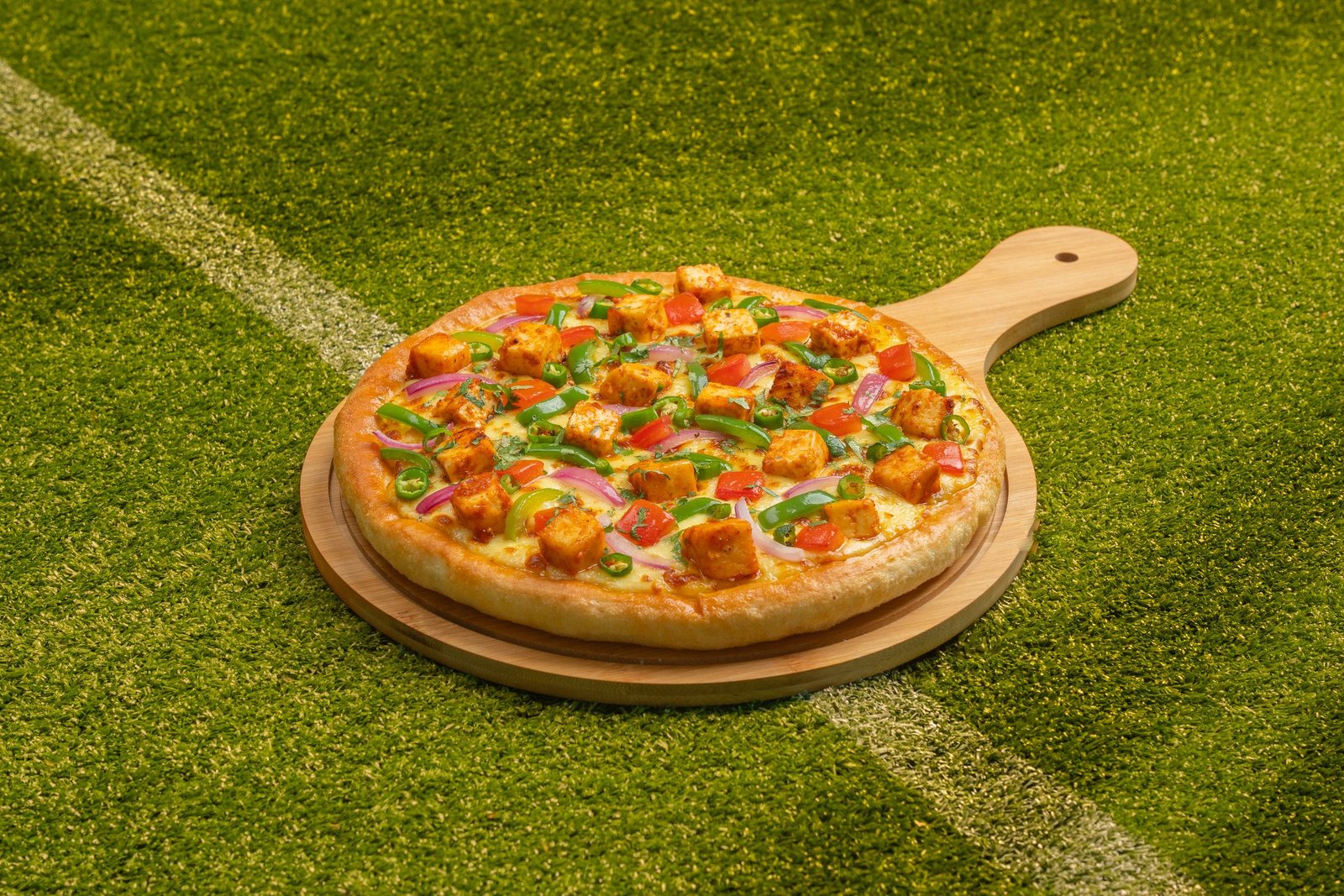 A single pan pizza on a wooden paddle on the crease line of a cricket pitch