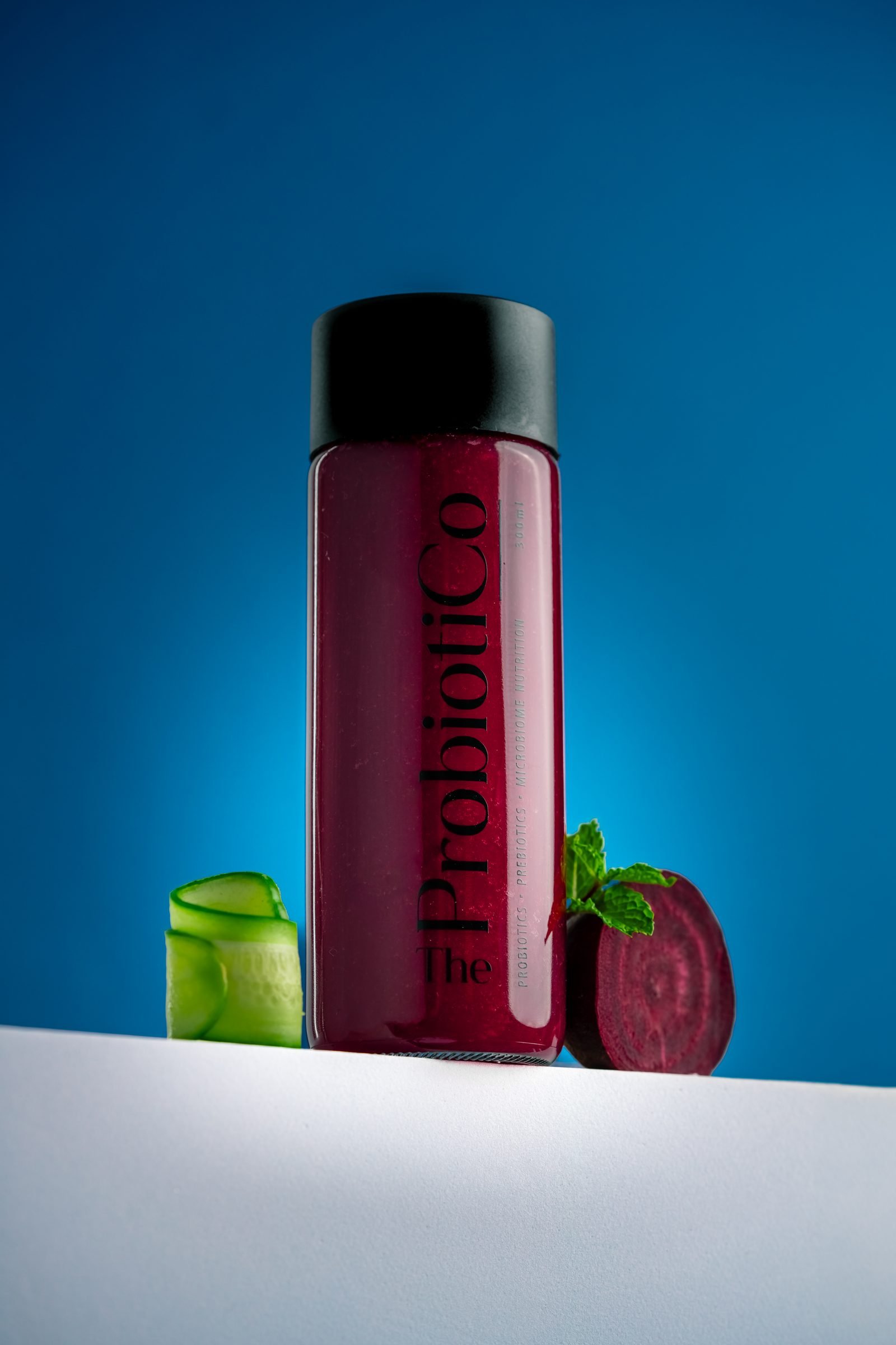 Bottle of beetroot Probiotico juice beside a cut beetroot and a green apple, on blue