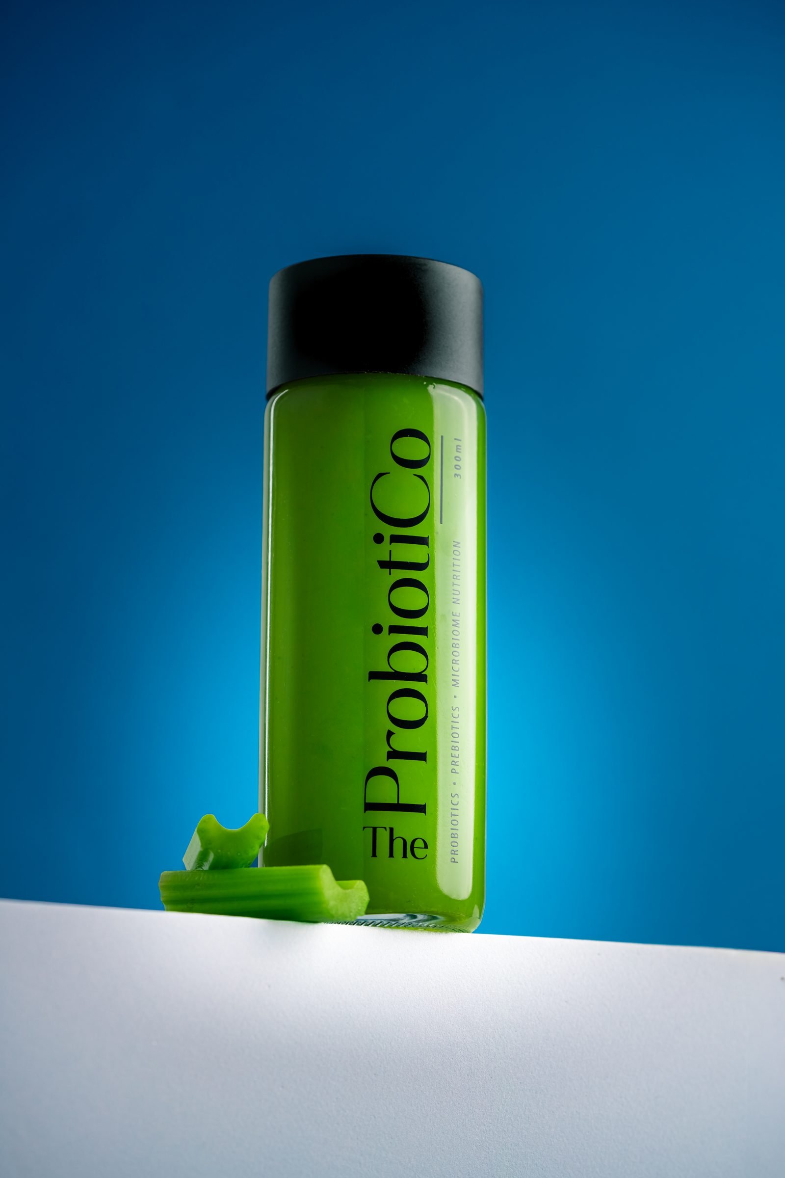 Bottle of green Probiotico juice with a celery stick at its base, on blue