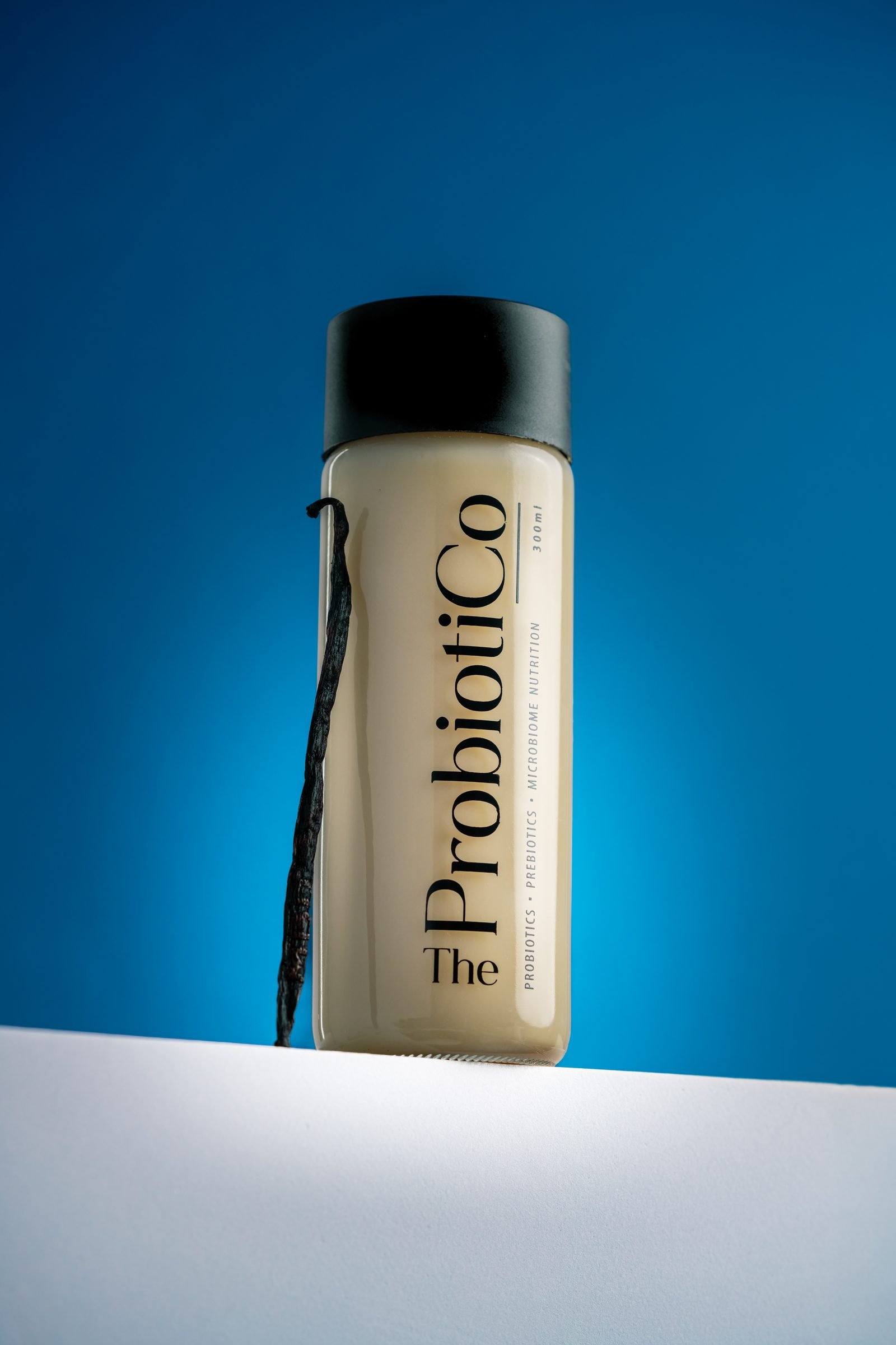 Bottle of vanilla Probiotico drink with a vanilla pod leaning against it, on blue