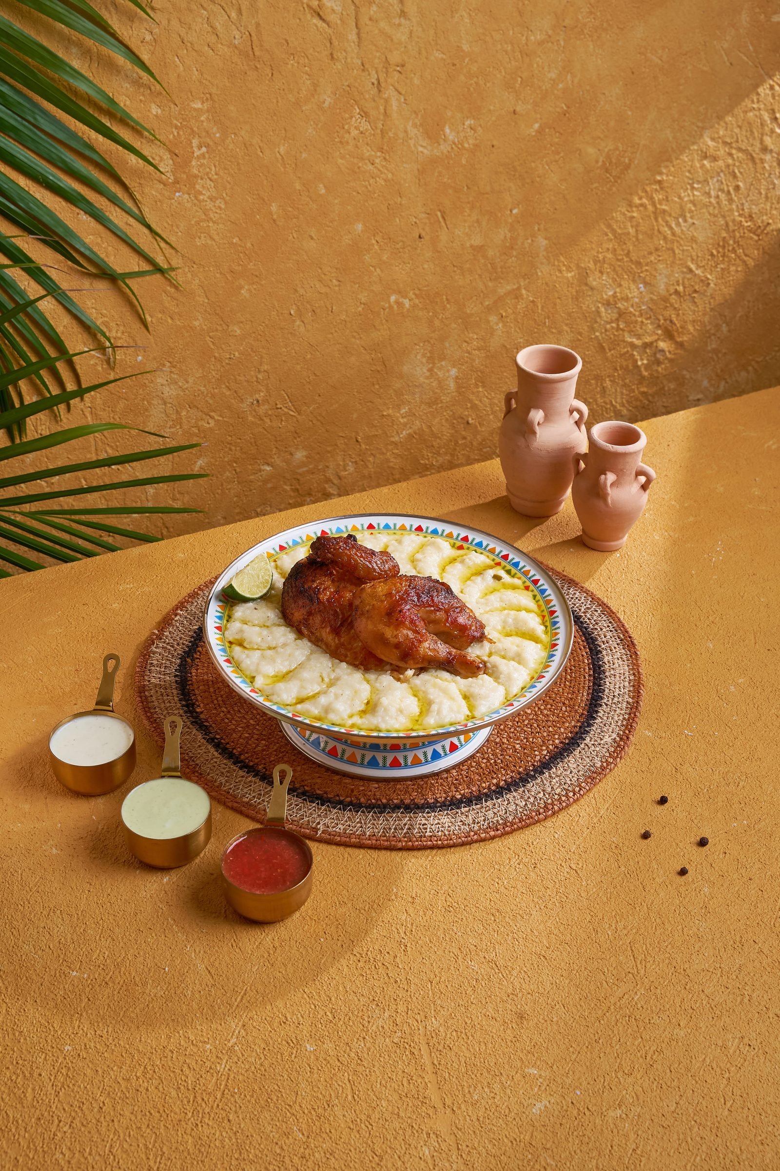 Roast chicken on white rice in a blue-rimmed bowl with clay jugs and palm fronds
