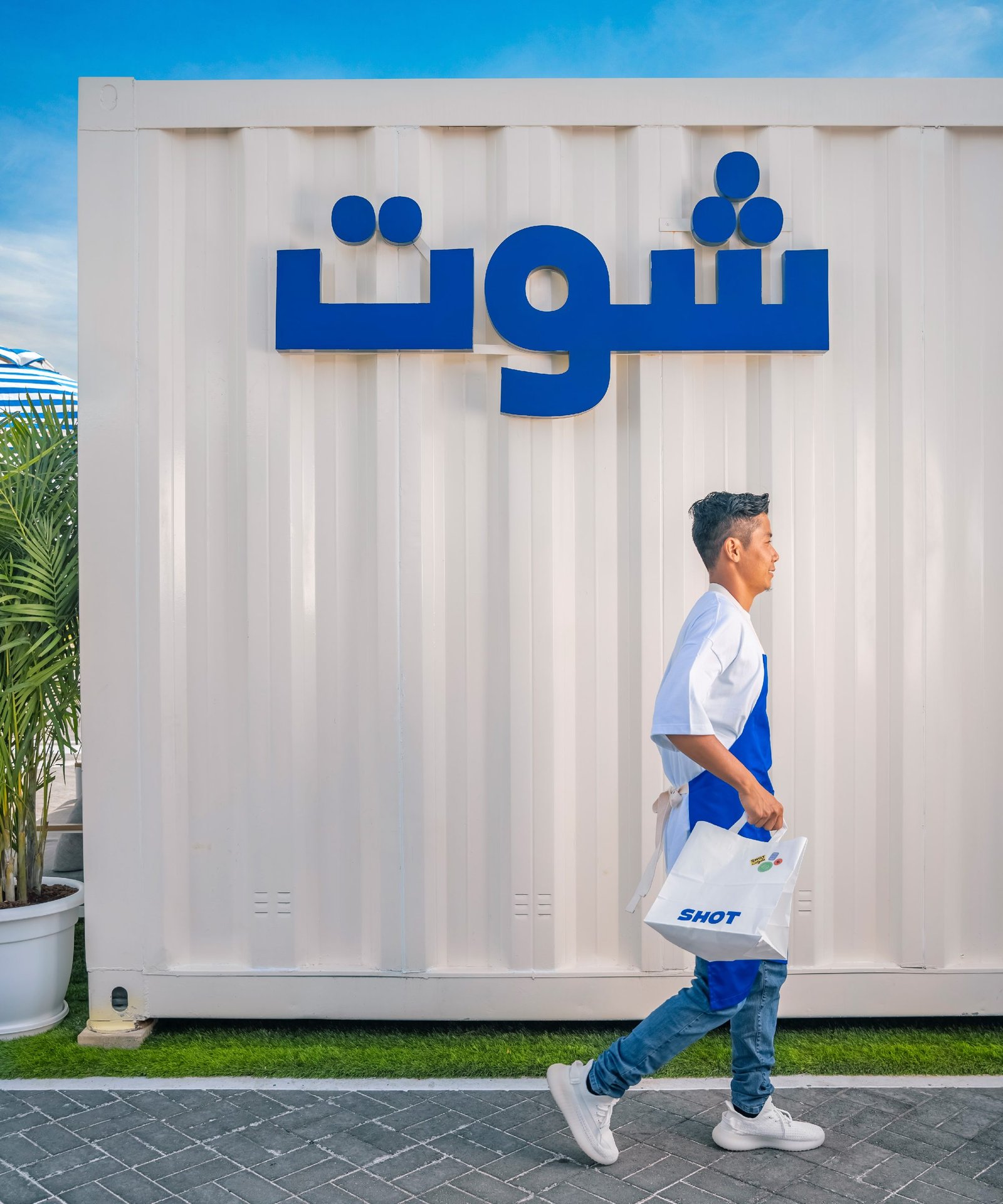 Man in a Shot apron walking past a white container painted with the brand's Arabic wordmark