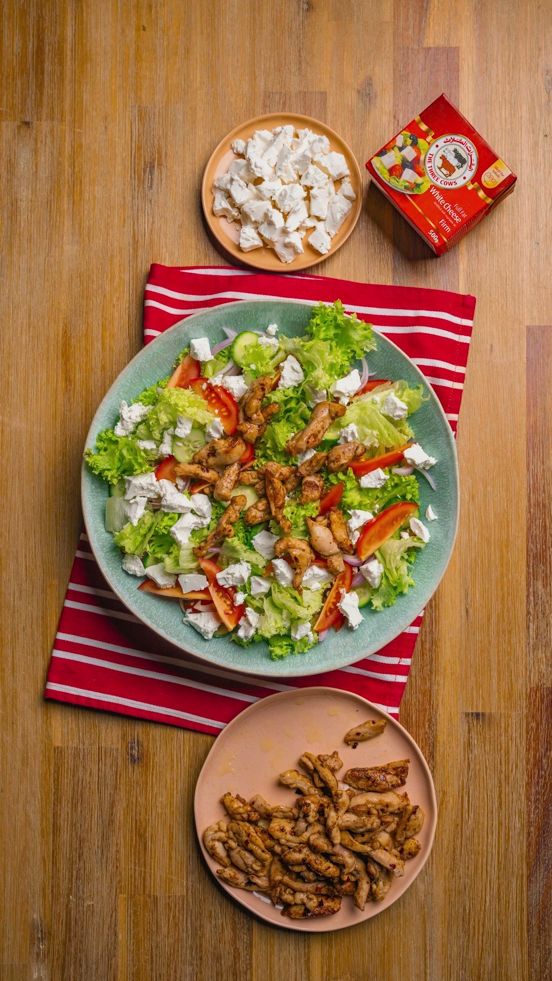 Overhead of a chicken and feta salad on a wooden table with a red striped runner
