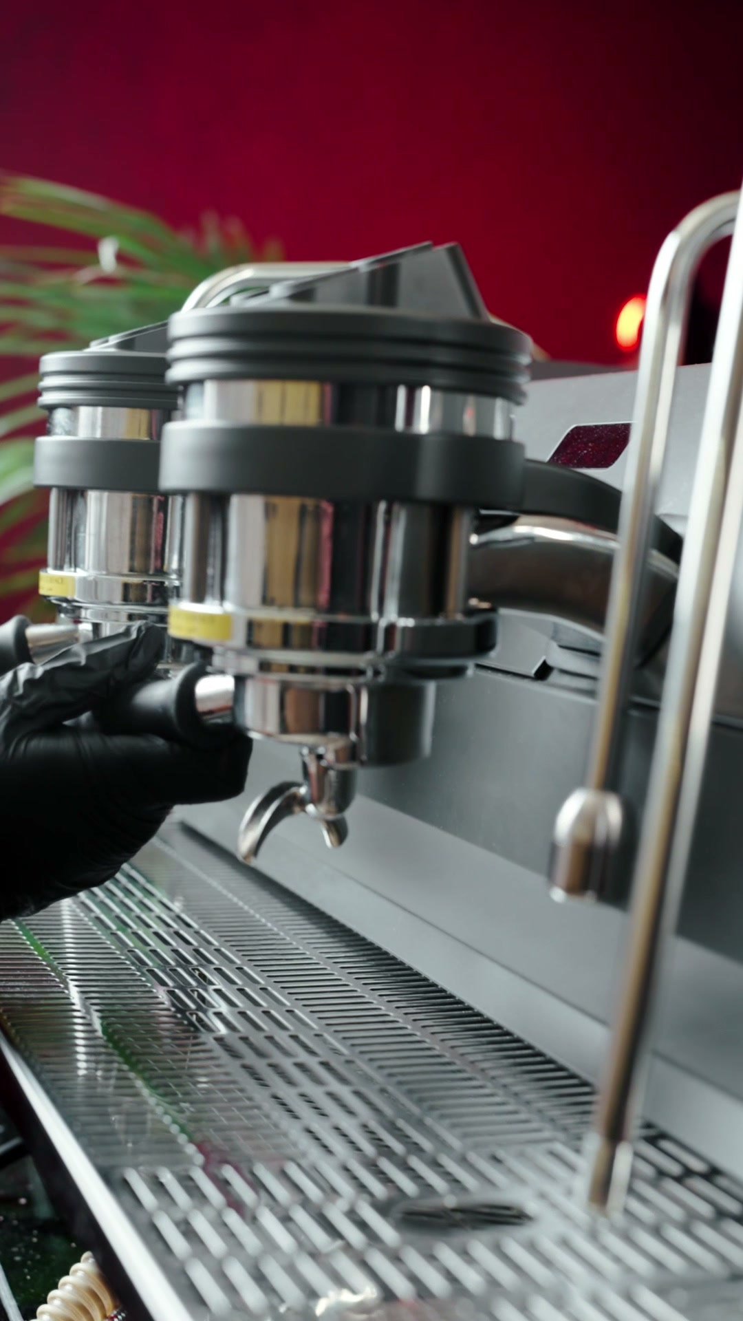 Chrome espresso machine group heads close up against a red-lit cafe interior