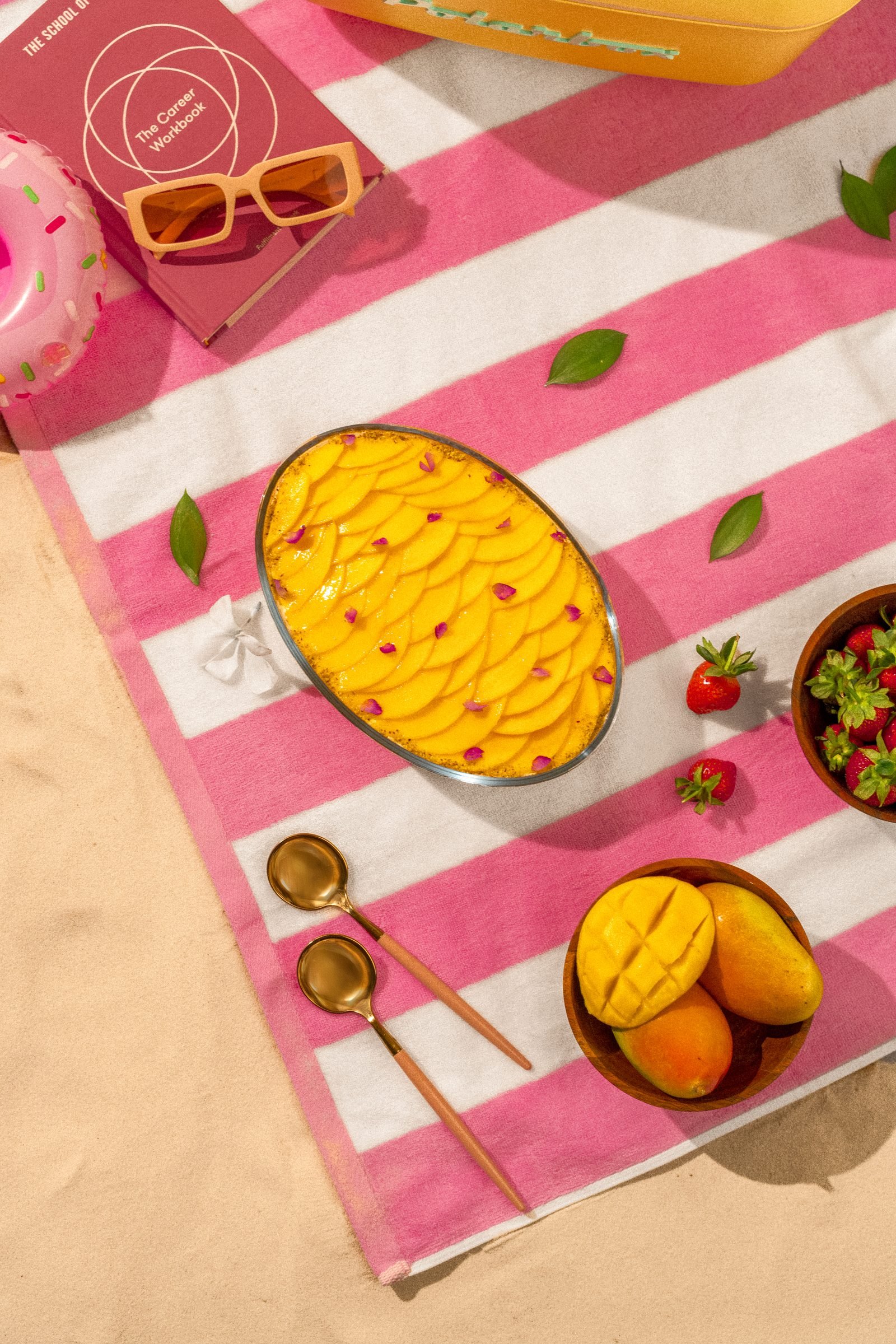 Overhead of a mango tart on a pink striped beach towel with sunglasses and berries
