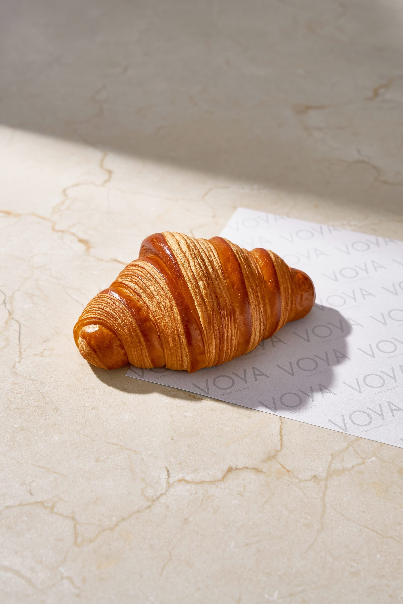 Butter croissant on Voya paper on cream marble, in hard sunlight