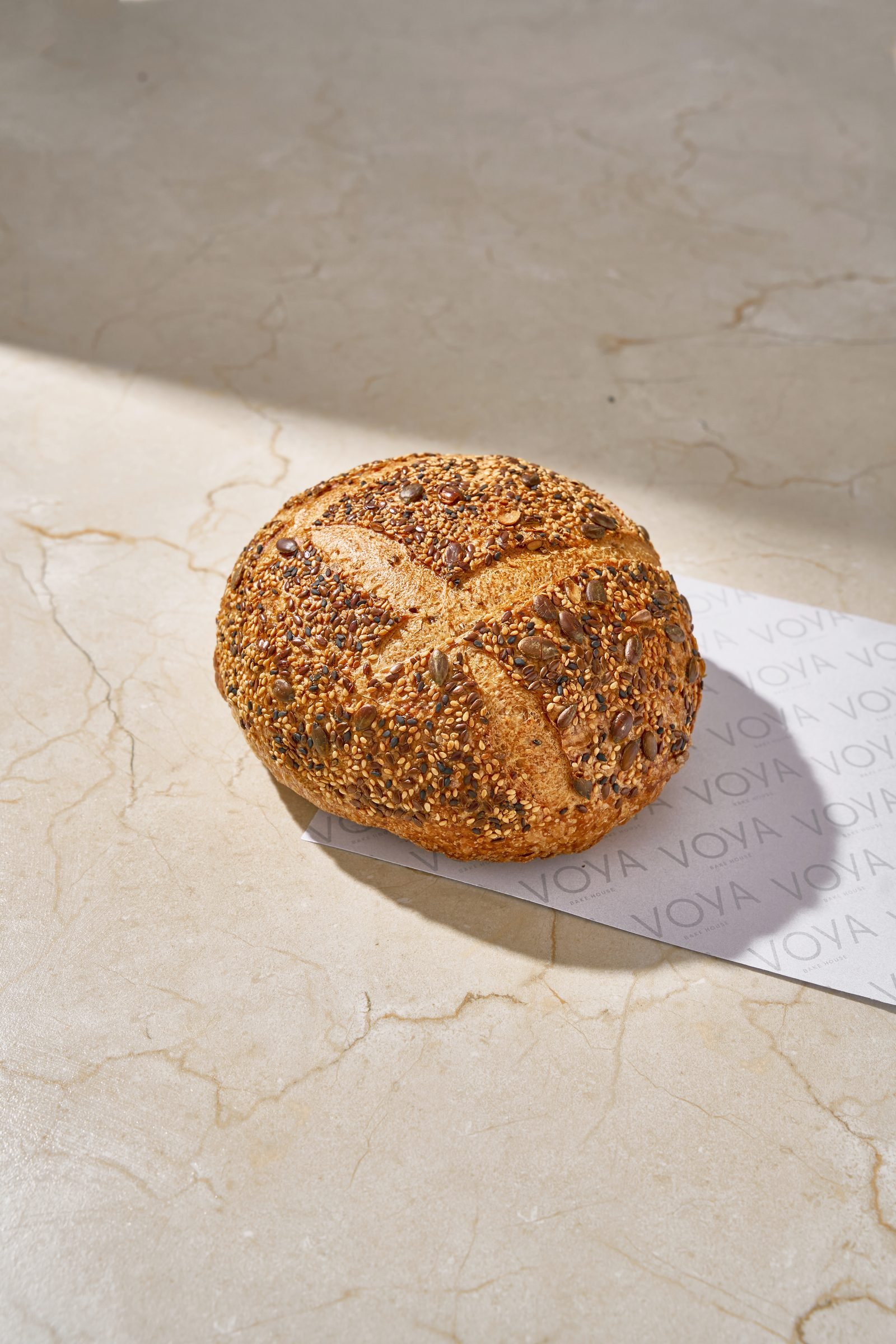 Seeded sourdough round scored with a cross, on Voya paper on cream marble