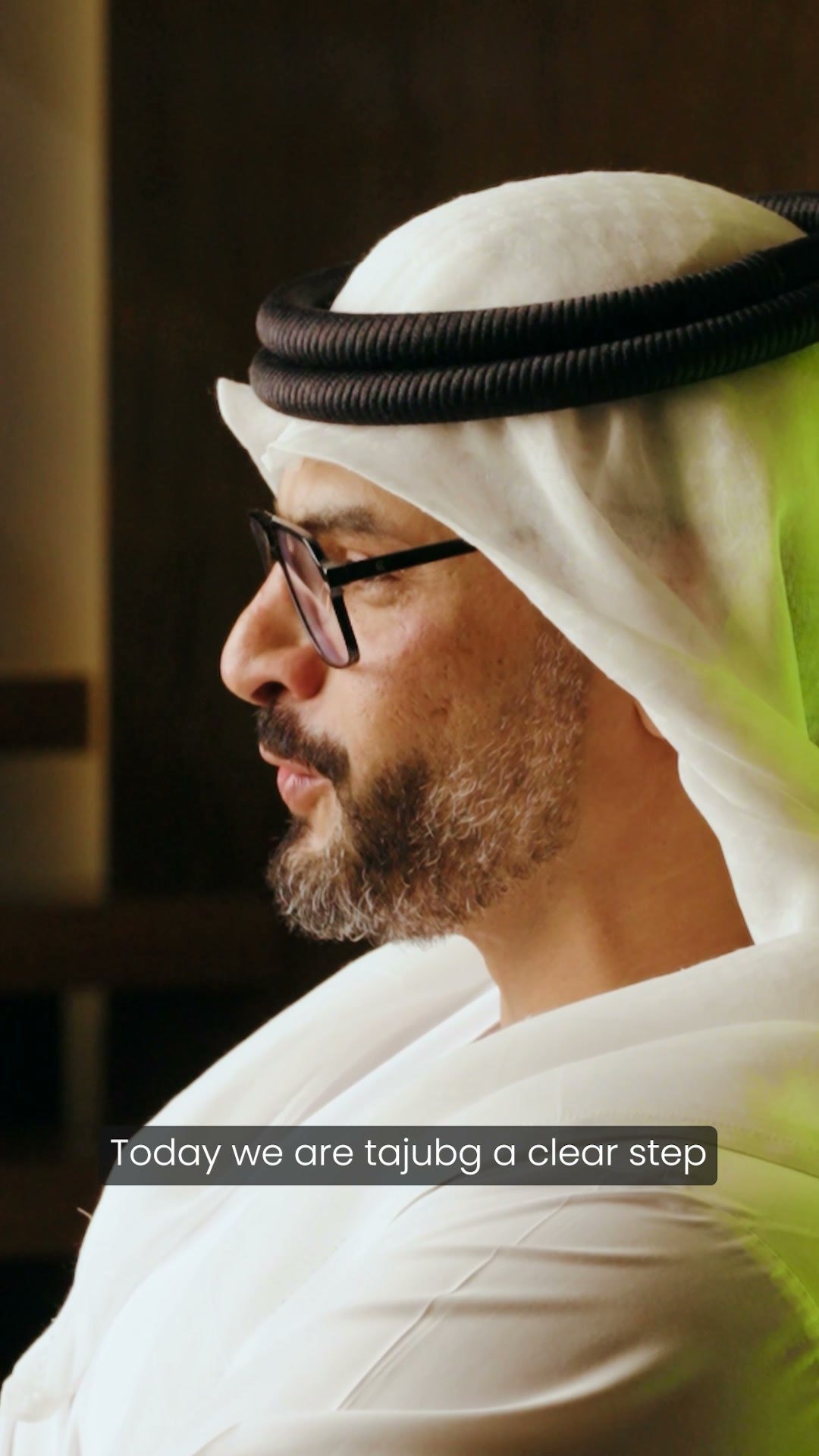 Man in a kandura and glasses in profile, a subtitle line across the lower frame