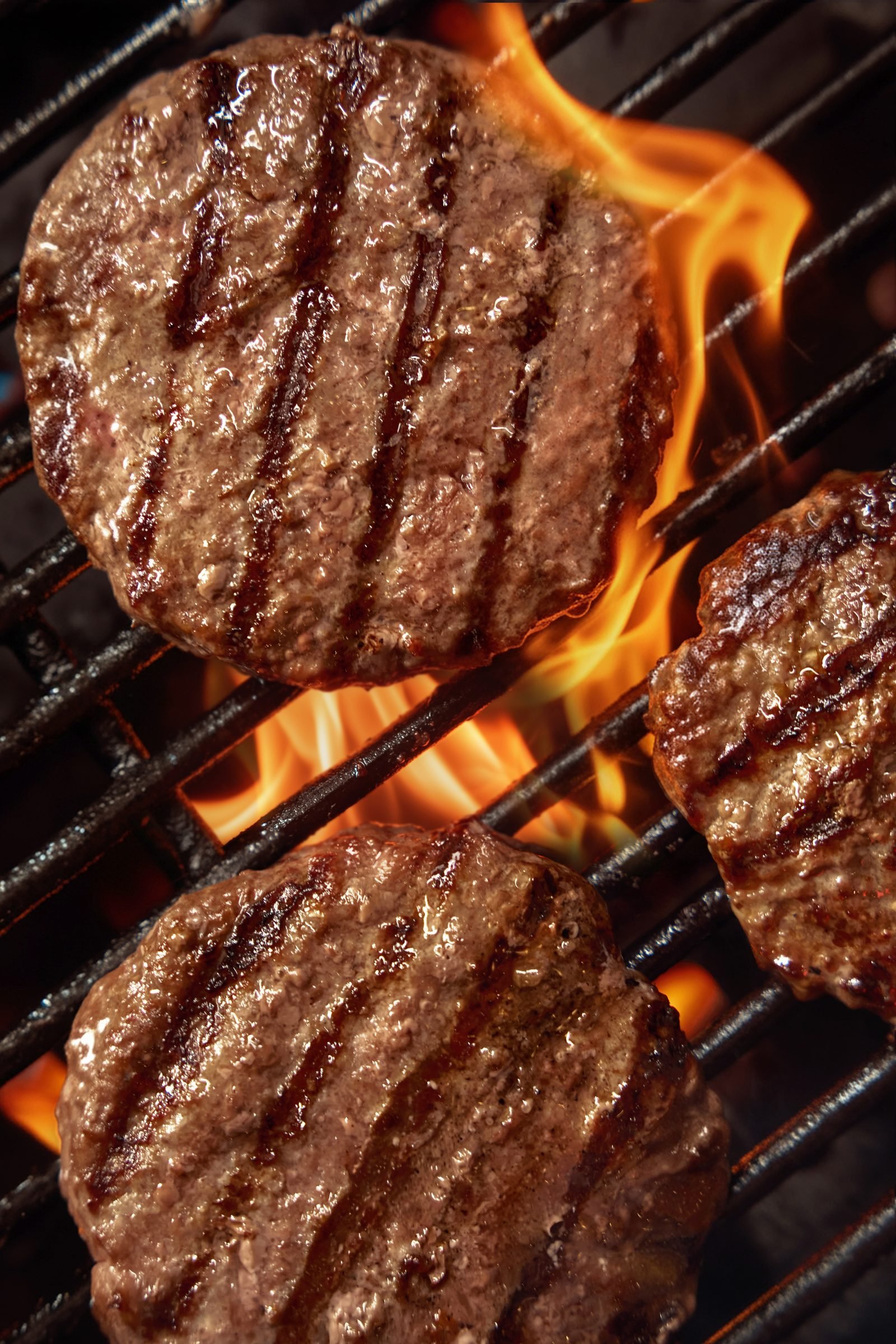 Beef patties searing over open flames on a grill