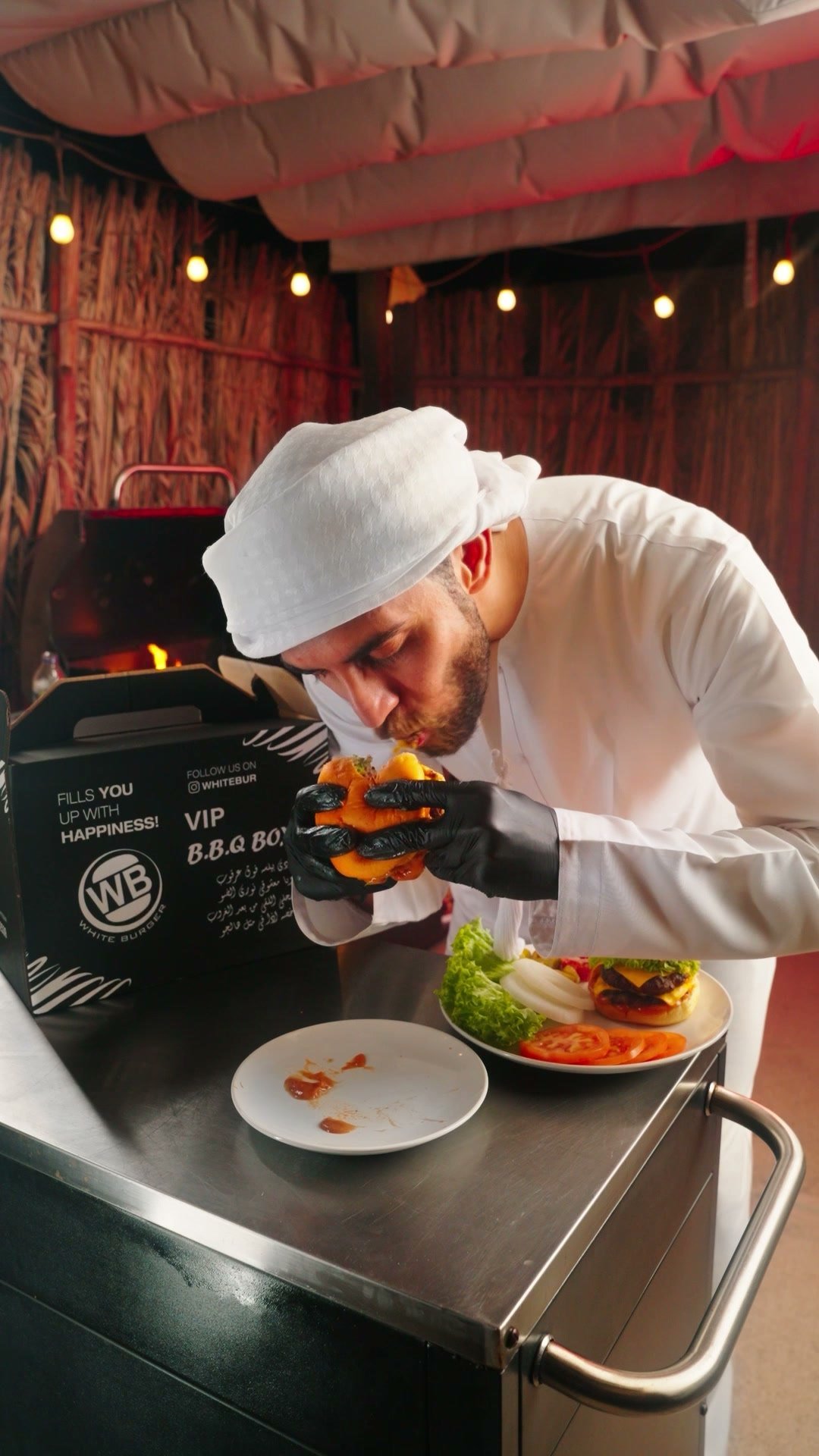 Chef in whites plating a dish on a steel counter beside a White Burger service window